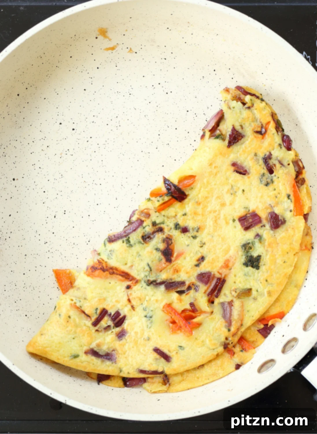 Close-up of a vibrant Veggie Vegan Omelet sizzling in a white skillet, showcasing colorful vegetable fillings