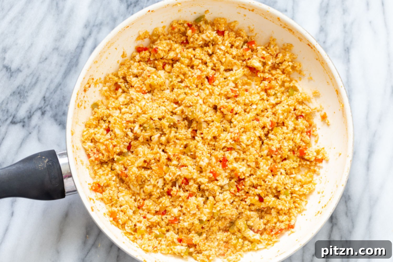 Spanish Cauliflower Rice cauliflower rice being added to a saucepan with bell pepper sauce to make Spanish Cauliflower Rice