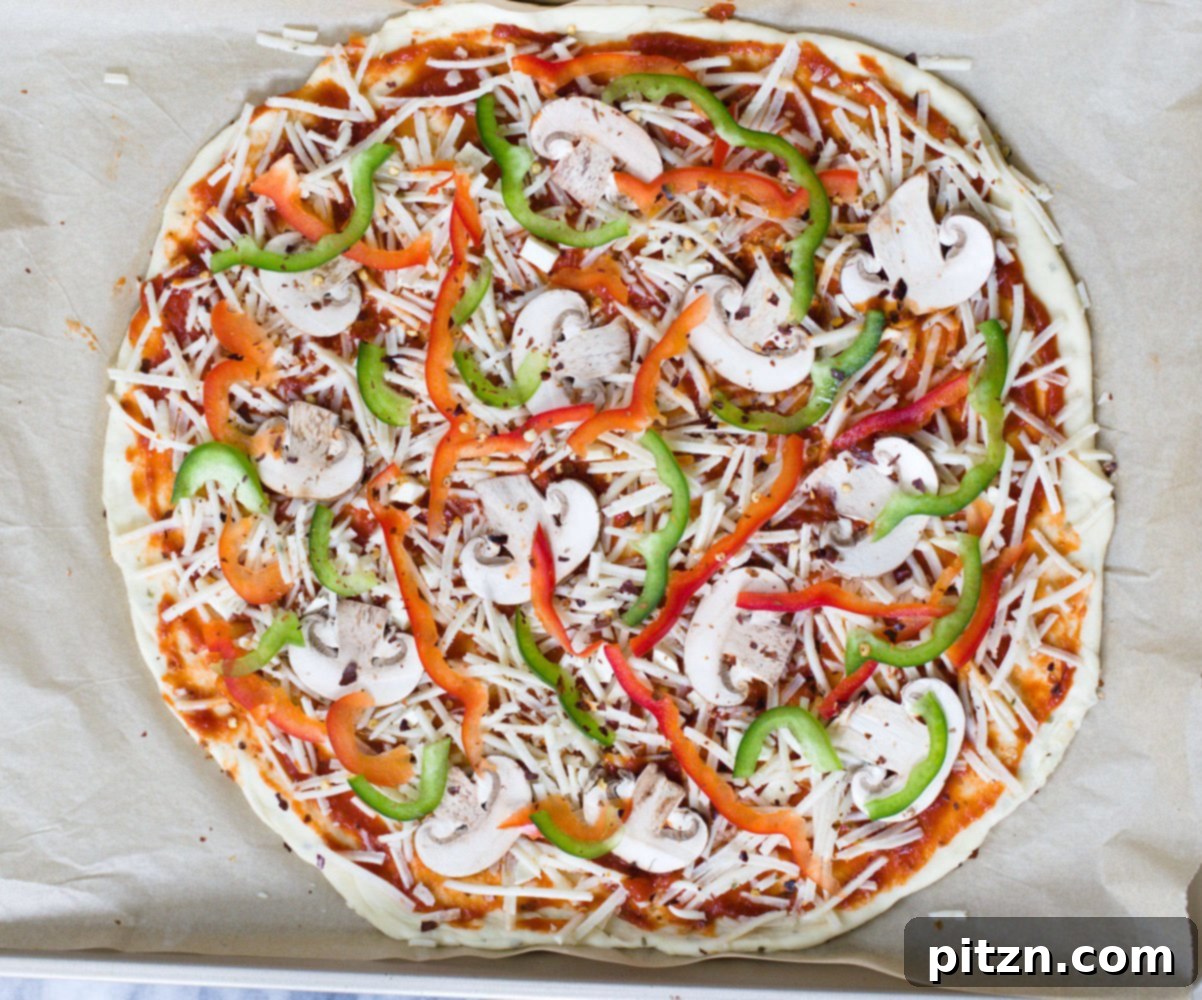 no yeast pizza dough overhead shot of unbaked vegan pizza on a baking sheet topped with vegetables and vegan cheese shreds