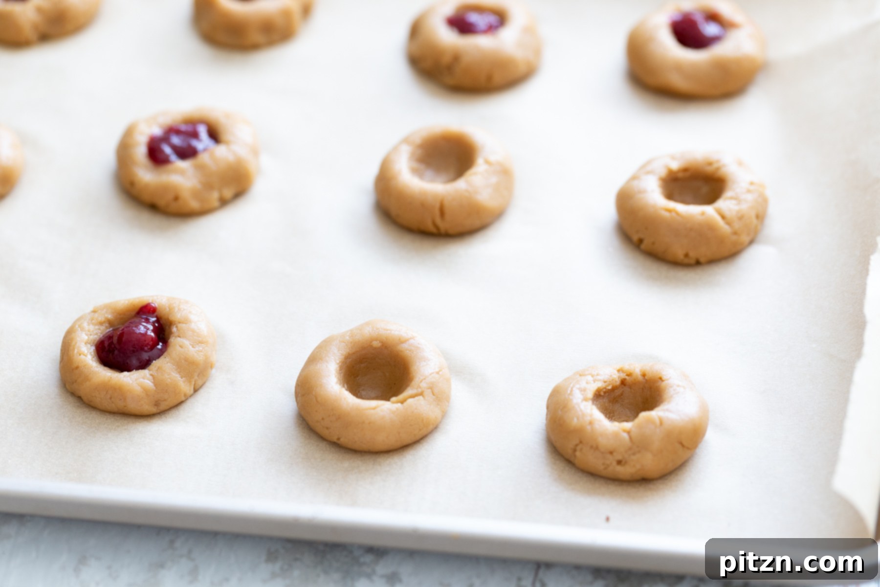 cookie dough balls being indented and filled with jam to make thumbprint cookies