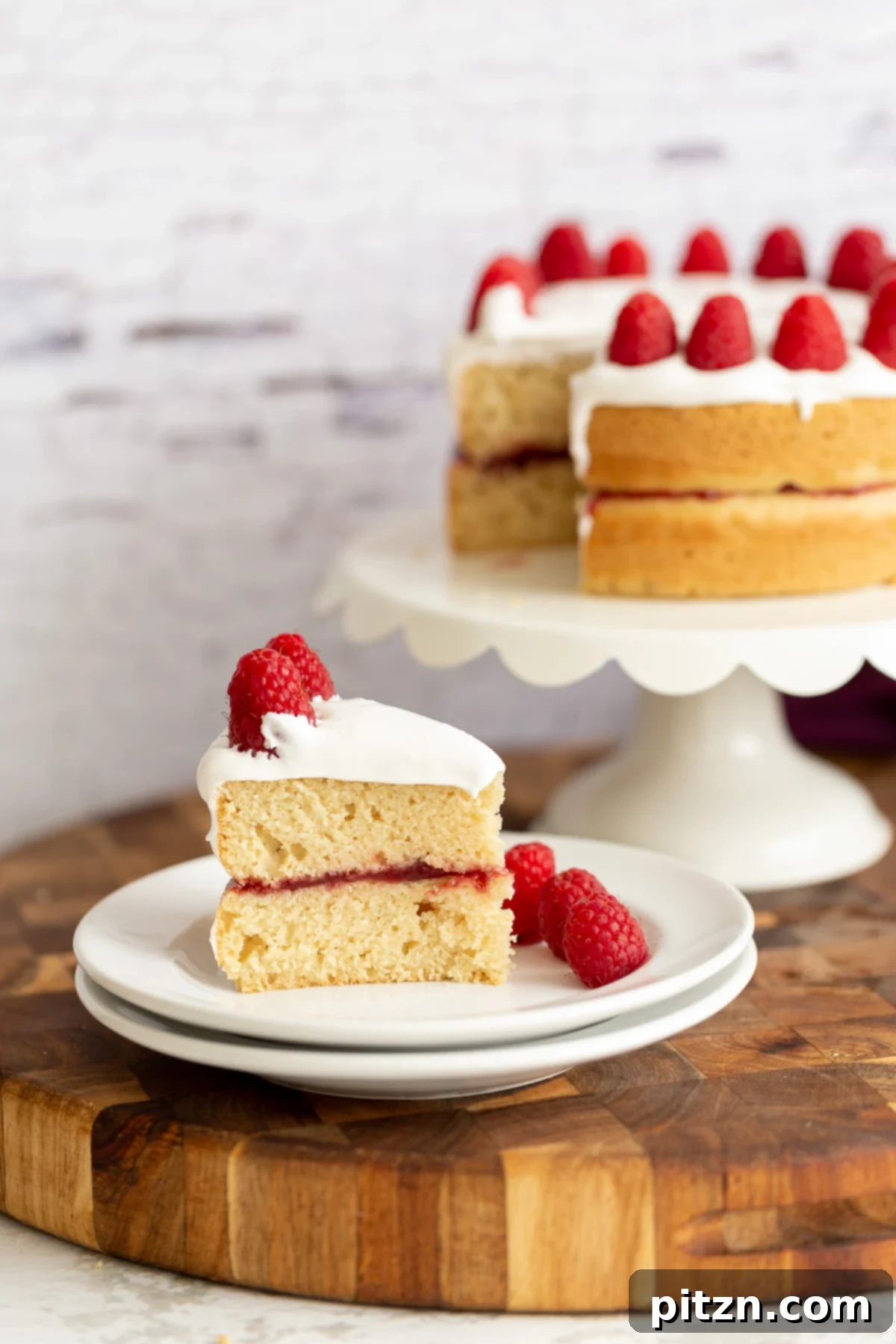A beautiful slice of vegan white cake revealing layers of fluffy cake, raspberry preserves, and coconut whipped cream topping.