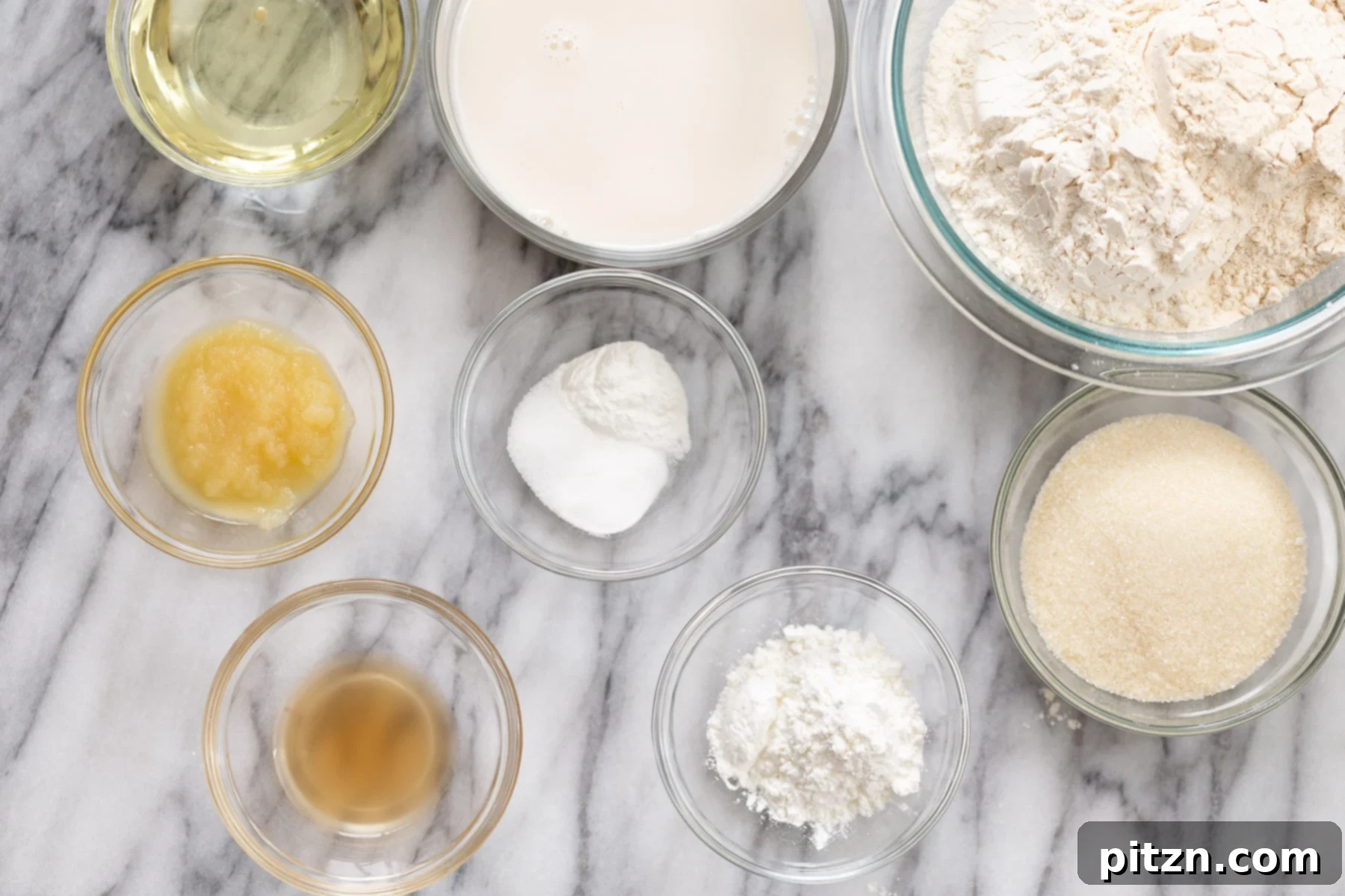 A display of all the fresh ingredients required to make the vegan white cake, neatly arranged on a pristine marble kitchen counter.