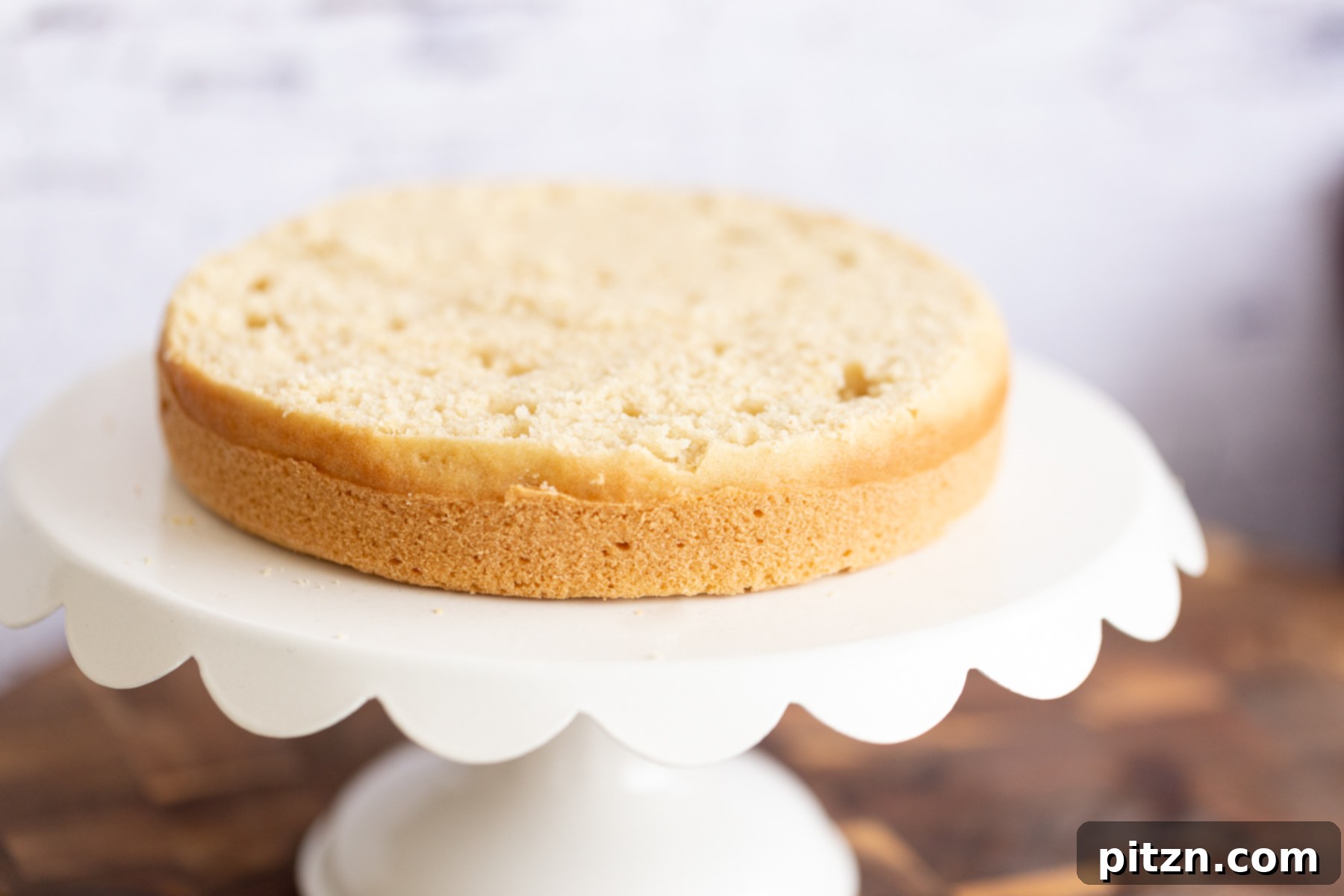 One leveled half of a vegan white cake placed on a cake stand, prepared for assembly into a multi-layer cake.
