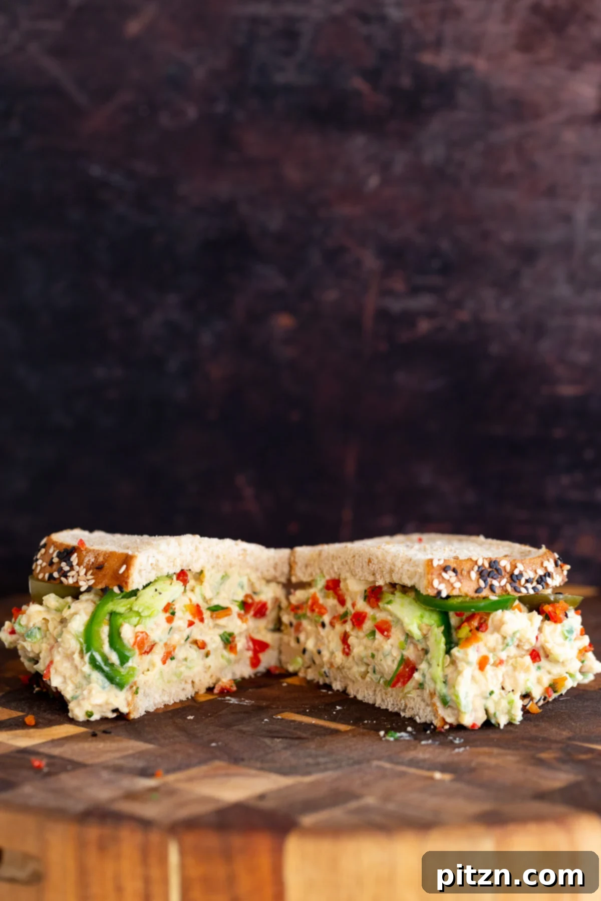 Hearty Plant-Based Chickpea Salad Sandwich Half of a vegan Jalapeño Popper Chickpea Salad Sandwich, cut diagonally and served on a rustic wooden chopping board.