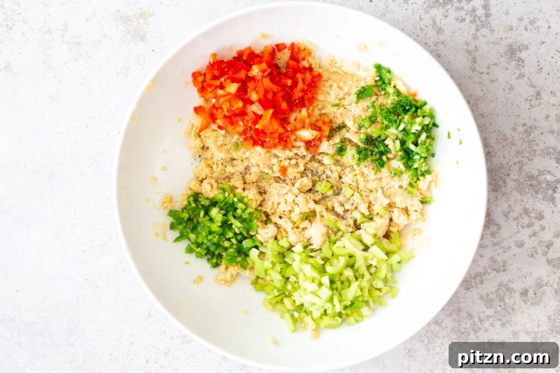 Assembled Chickpea Salad Components All vegan chickpea salad ingredients, including chopped vegetables and mashed chickpeas, assembled in a white bowl before mixing.