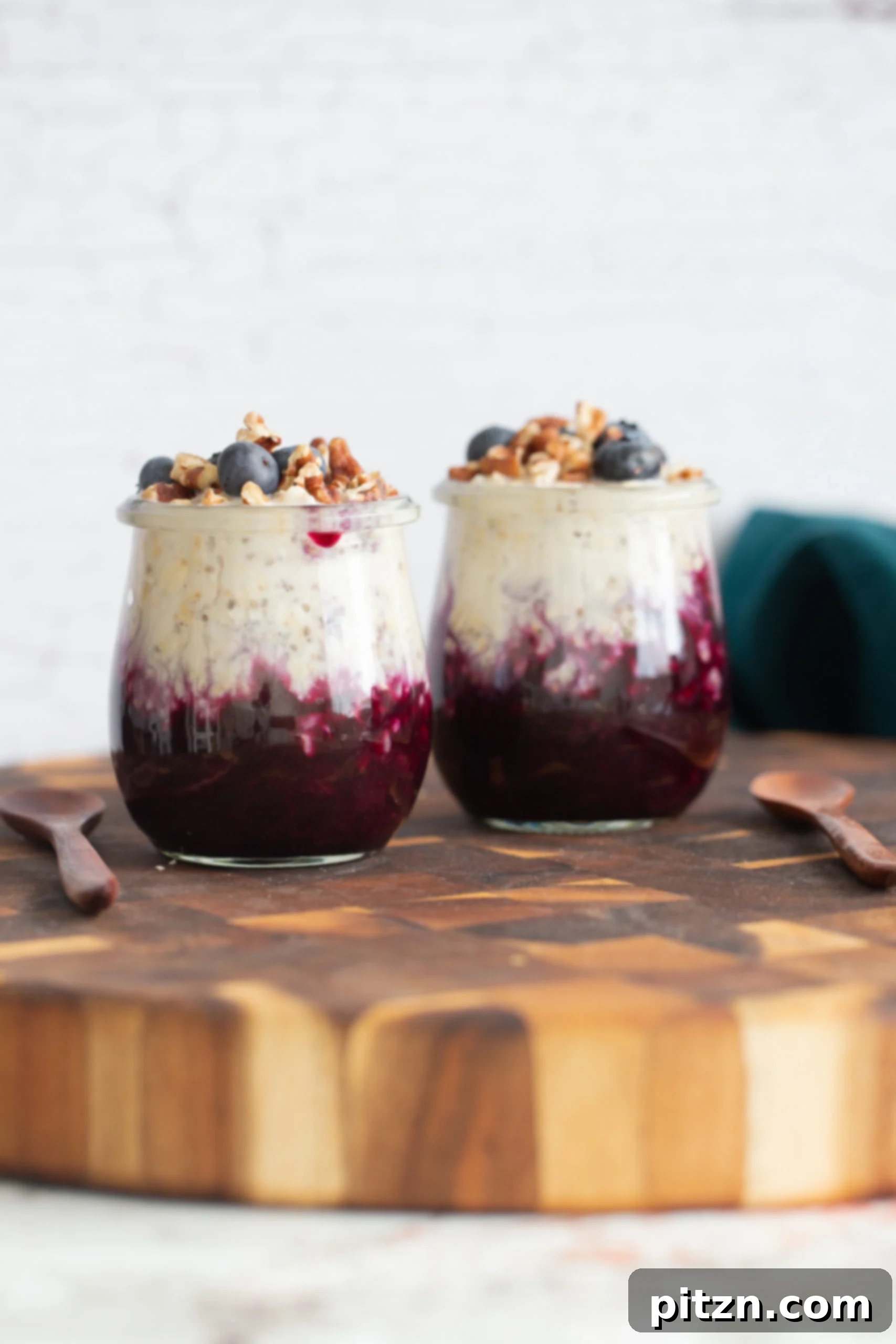 Vegan Blueberry Muffin Overnight Oats Two jars of make-ahead vegan blueberry muffin overnight oats on a rustic wooden board, garnished with fresh blueberries and a sprinkle of nuts, showcasing a vibrant purple hue