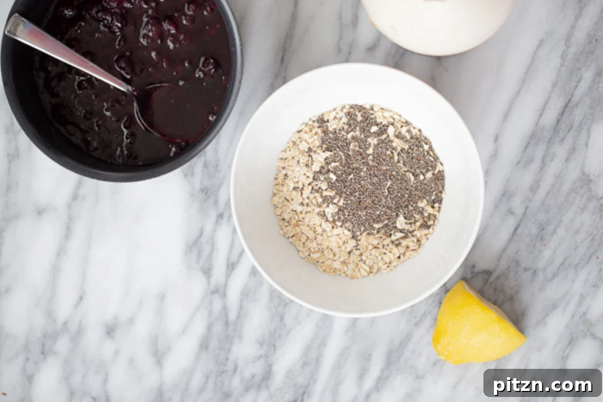 Blueberry Overnight Oats Ingredients Overhead shot of two bowls: one contains dry oats and chia seeds, while the other holds a vibrant purple blueberry compote, ready for mixing to create overnight oats