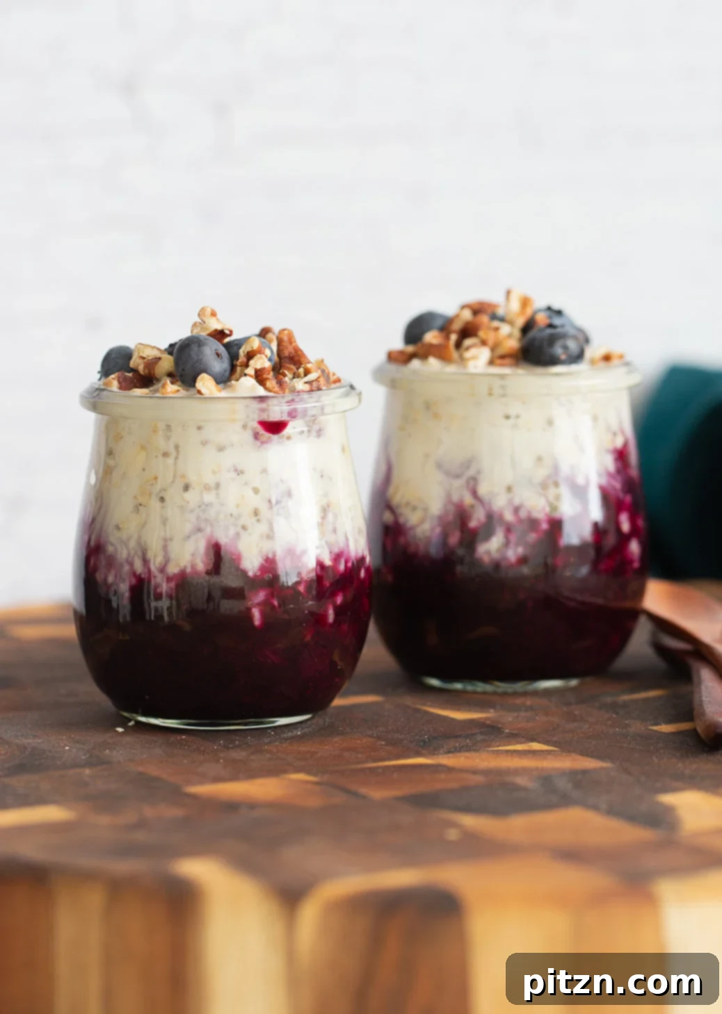 Blueberry Muffin Overnight Oats Jars Small mason jars filled with layered blueberry muffin overnight oats, topped with vibrant blueberries and crunchy chopped pecans, ready to be enjoyed