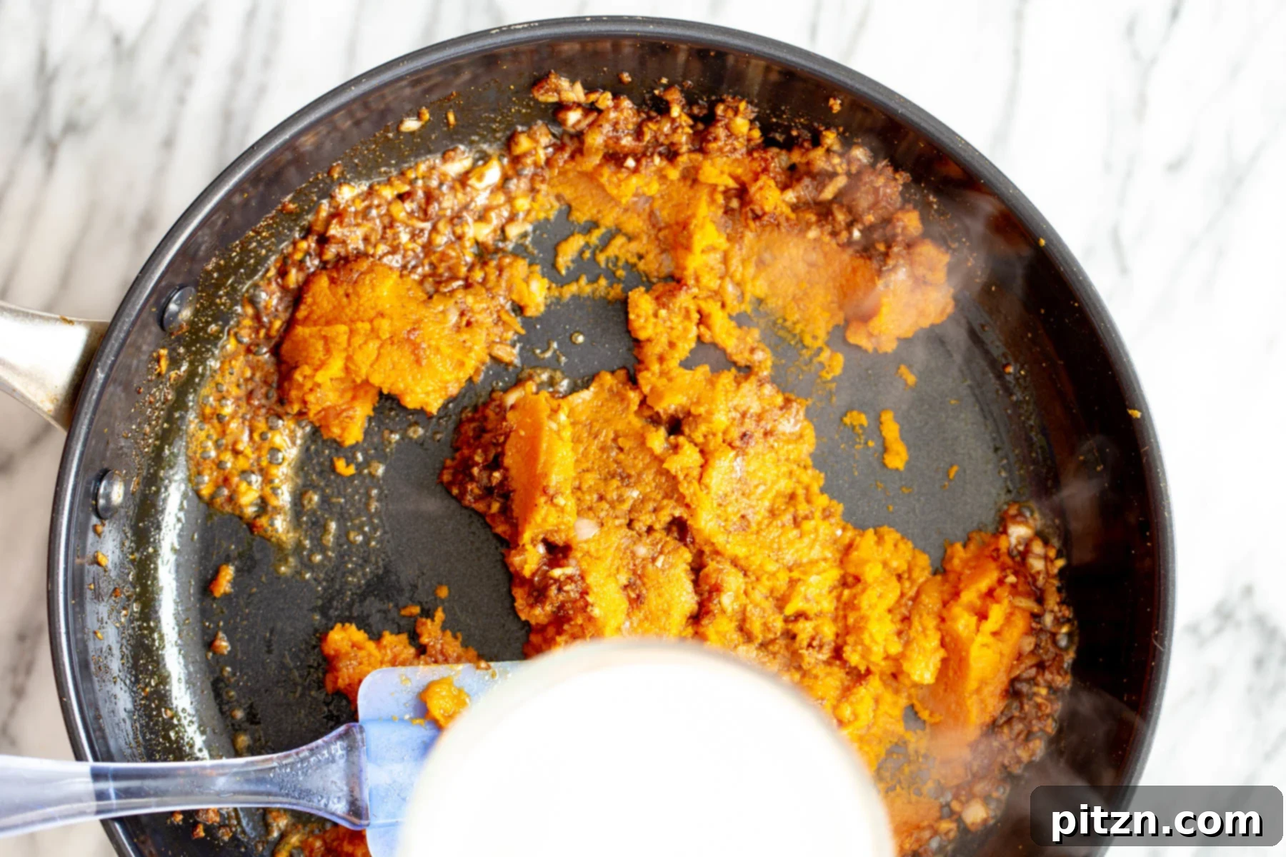 Adding Pumpkin Puree Smooth pumpkin puree being added to the pan with tempered Indian spices and aromatics, beginning the creamy sauce.