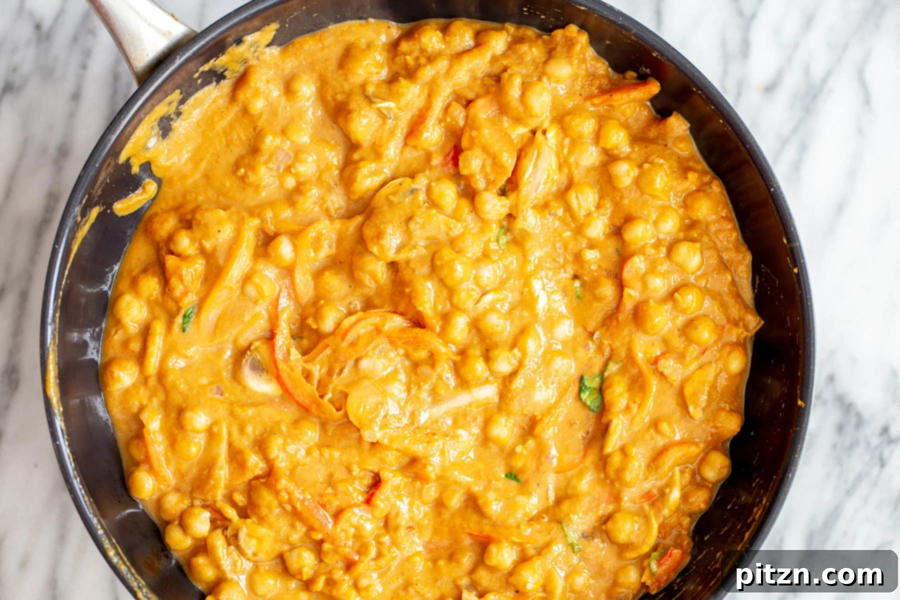 Chickpeas Cooking in Pumpkin Gravy Chickpeas and vegetables simmering in the rich, orange pumpkin gravy within a skillet, creating a delicious curry.