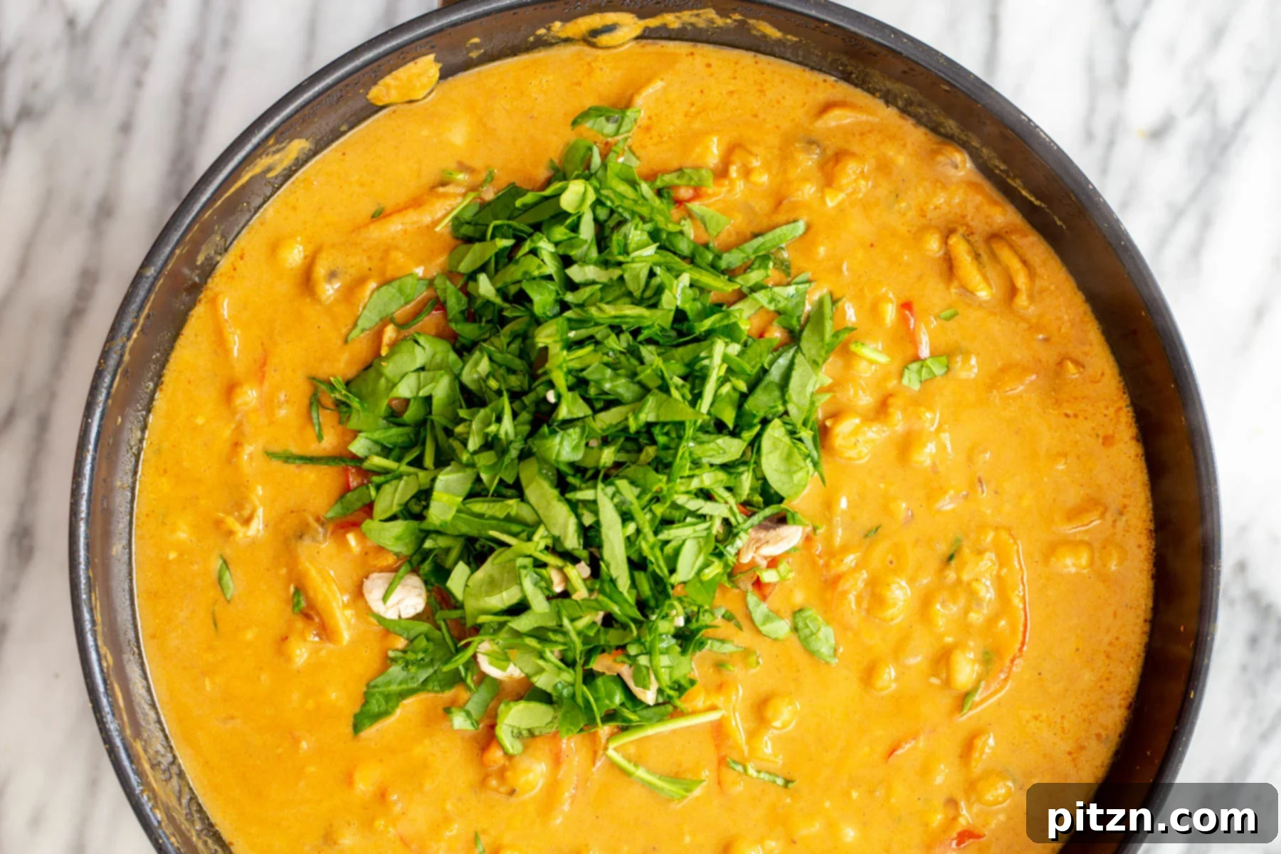 Garnished Pumpkin Curry Close-up of pumpkin chickpea curry being garnished with fresh herbs and a sprinkle of chili flakes before serving.
