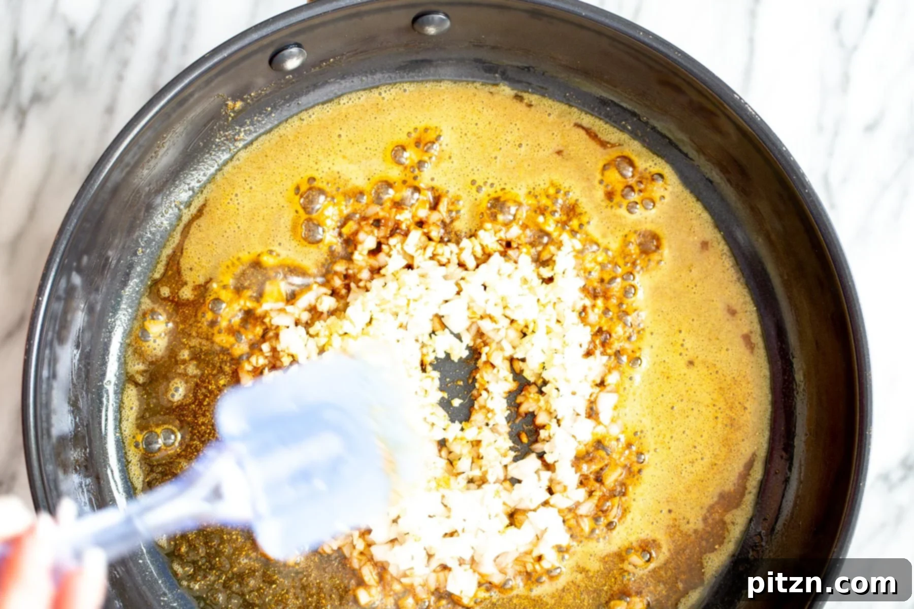 Curry Aromatic Base Overhead view of a skillet showing fried spices mingled with softened onions, garlic, and ginger, forming the aromatic base for the curry.