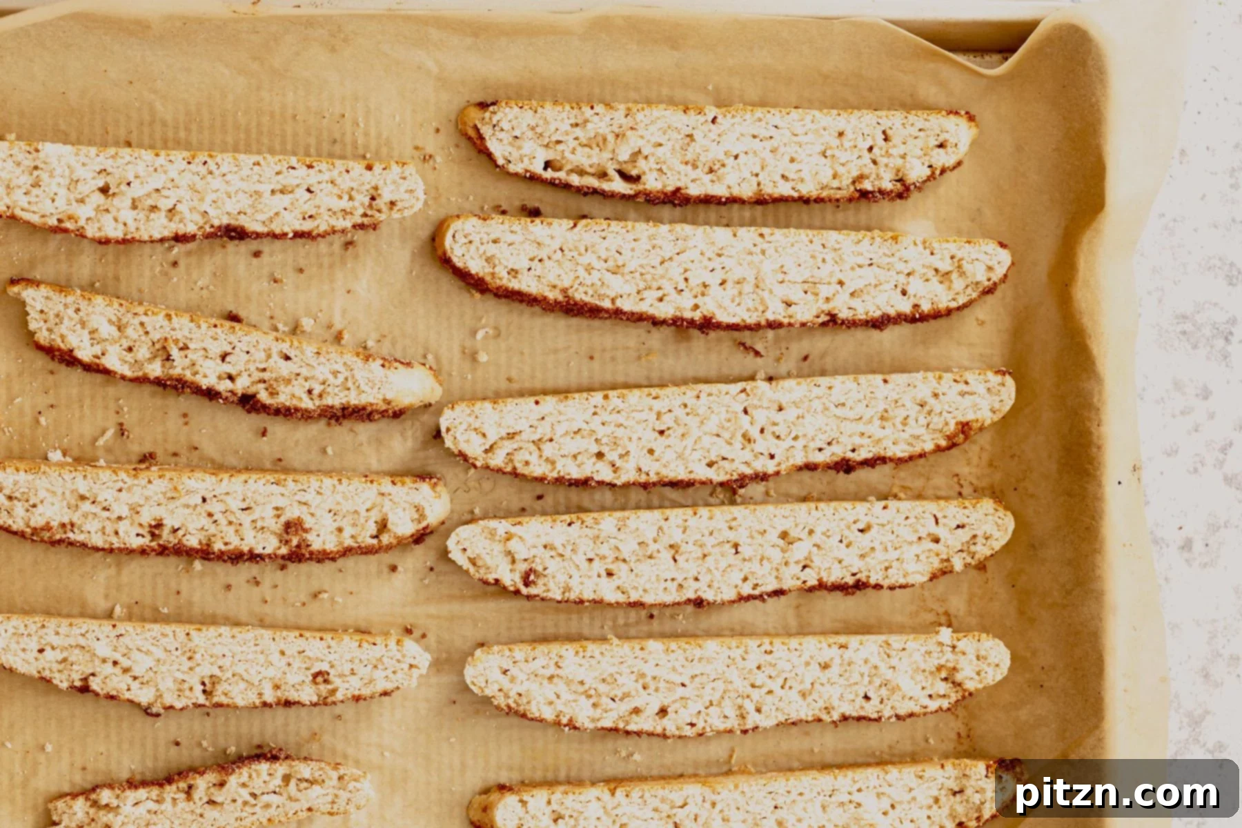 Individual slices of vegan cinnamon sugar biscotti are neatly arranged on a parchment-lined baking sheet, ready for their second bake.