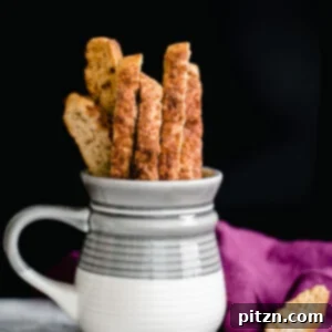 Close-up of a stack of Vegan Churro Biscotti, perfectly golden and coated in cinnamon sugar, next to a fresh cup of coffee.