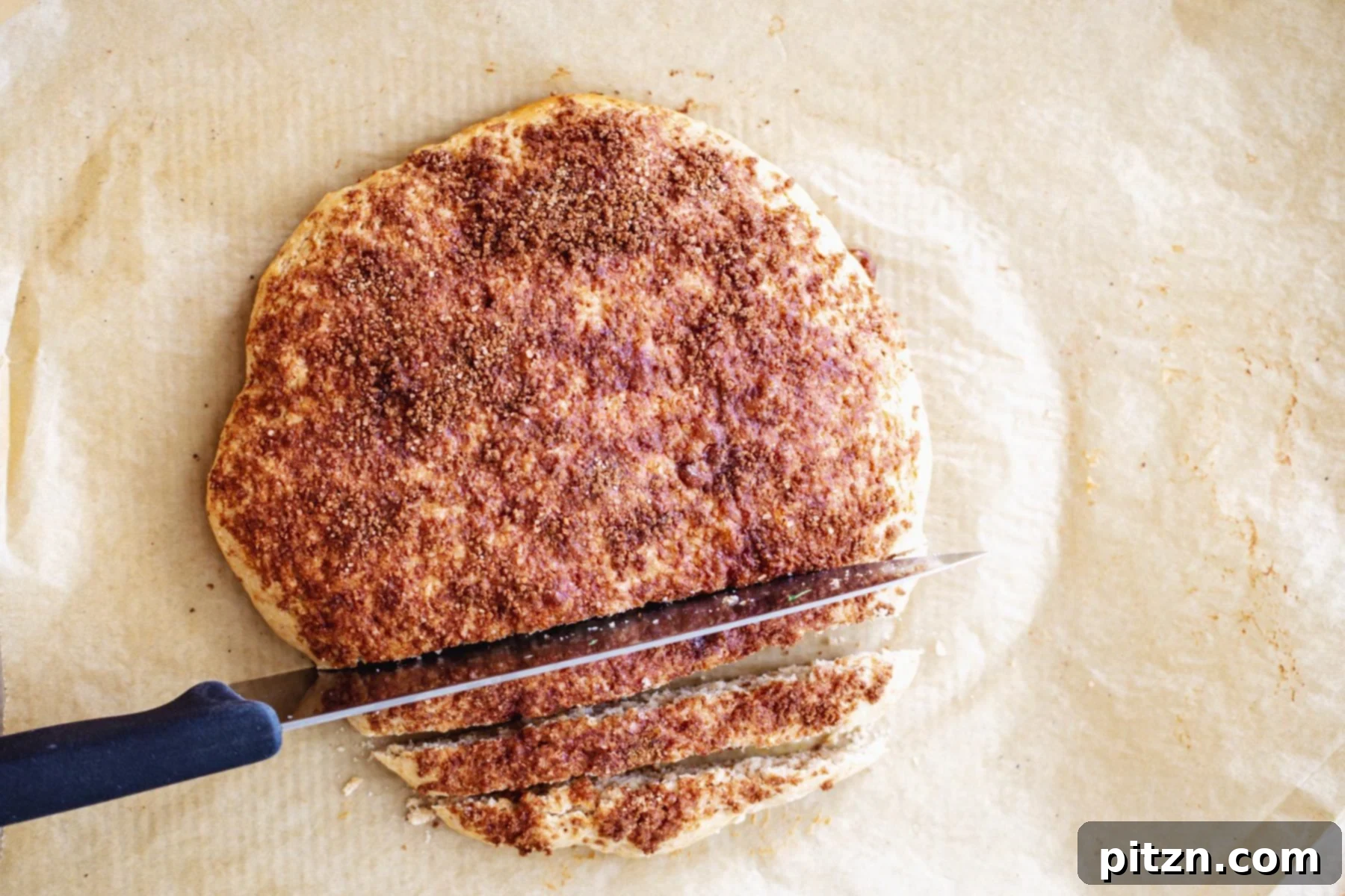 A baked vegan biscotti loaf is being carefully sliced into individual cookies on a cutting board with a serrated knife.