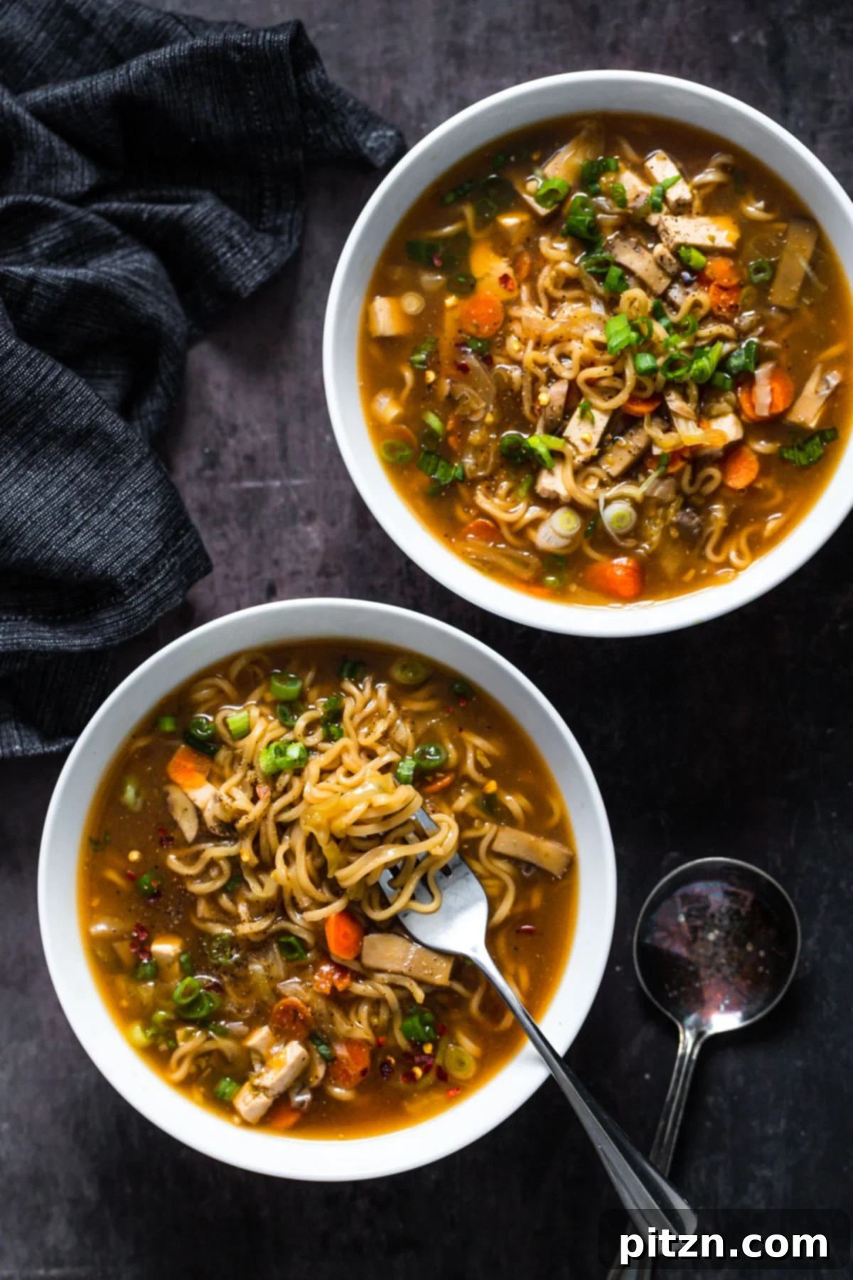 Vegan Hot and Sour Ramen Bowl 2 Two bowls of steaming Vegan Hot and Sour Soup with Ramen noodles, garnished with fresh herbs and chili flakes, ready to be served on a dark surface.