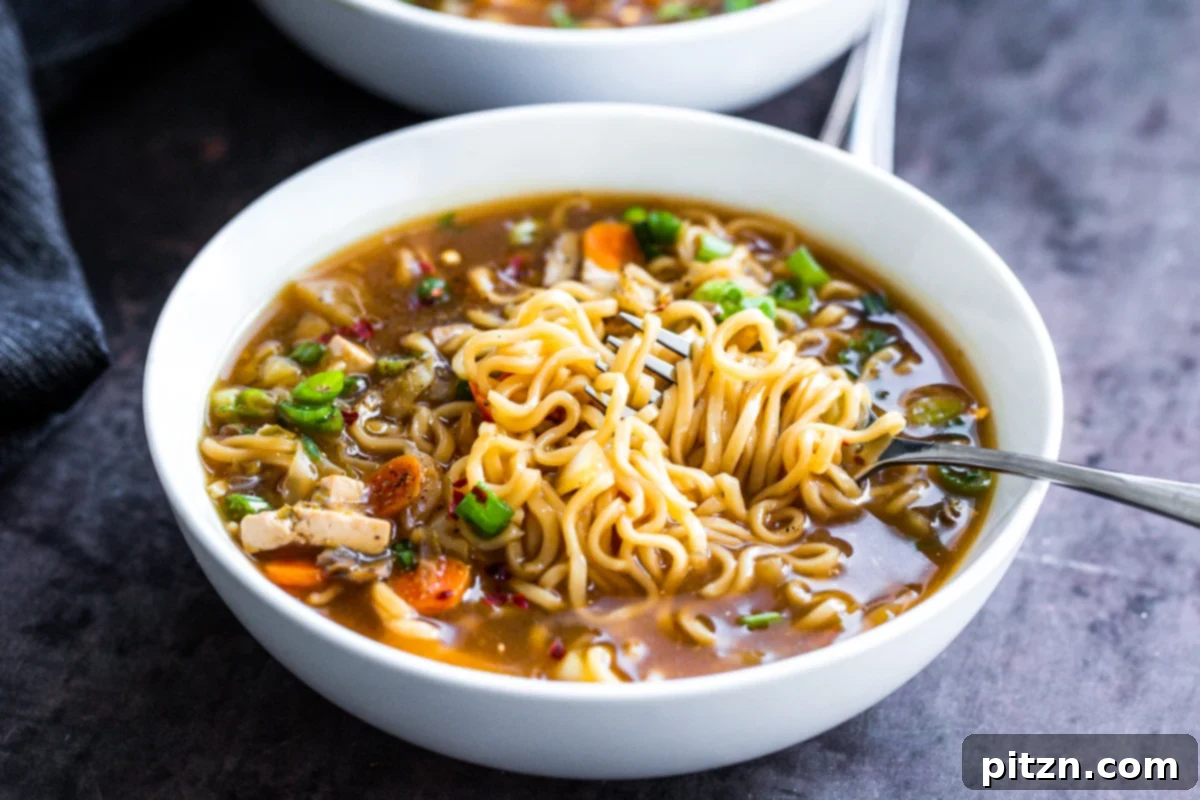 Vegan Hot and Sour Ramen Bowl 3 A fork lifts a generous swirl of ramen noodles from a steaming bowl of Vegan Hot and Sour Soup, highlighting the rich broth and vibrant ingredients.