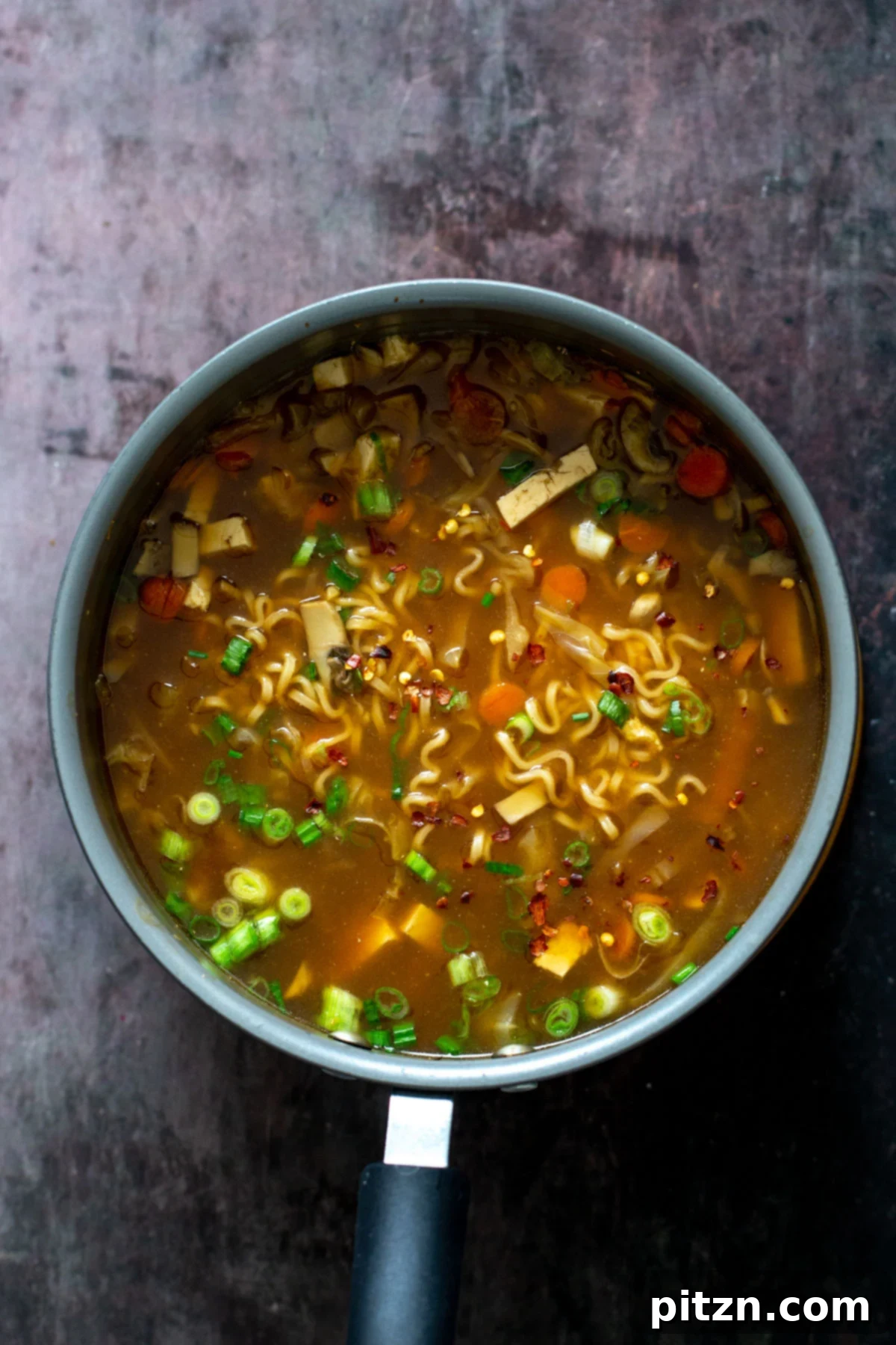 Vegan Hot and Sour Ramen Bowl 4 An overhead shot shows a large pot filled with Vegan Hot and Sour Soup, simmering gently with ramen noodles, sliced mushrooms, and colorful vegetables.
