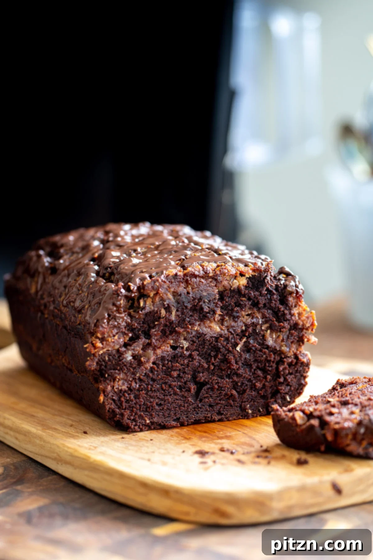 Vegan German Chocolate Loaf Cake - Classic Flavor, Easy Bake A beautifully sliced Vegan German chocolate loaf cake, revealing a dark chocolate cake with a distinct, golden-brown coconut pecan caramel swirl in the middle. One slice is cut out, ready to be enjoyed.