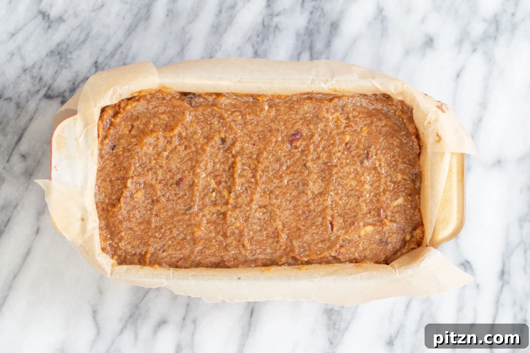 Coconut Pecan Chocolate Loaf 6 A close-up of half the chocolate cake batter spread evenly in a parchment-lined loaf pan, with a generous layer of the rich coconut pecan caramel swirl already dolloped on top, ready for more batter.