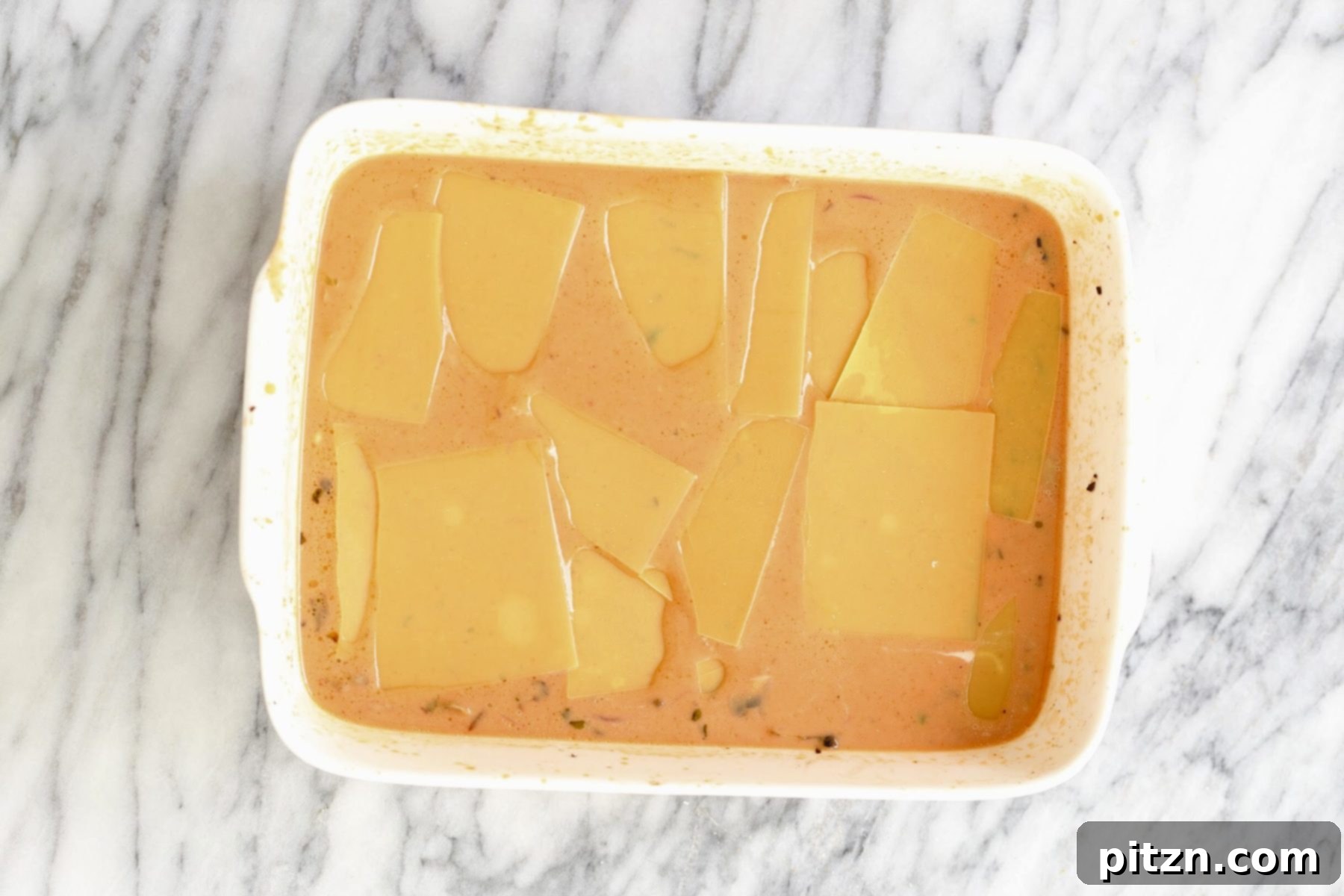 An unbaked vegan butter chicken lasagna in a casserole dish, with lasagna sheets submerged in the sauce, ready for the oven.