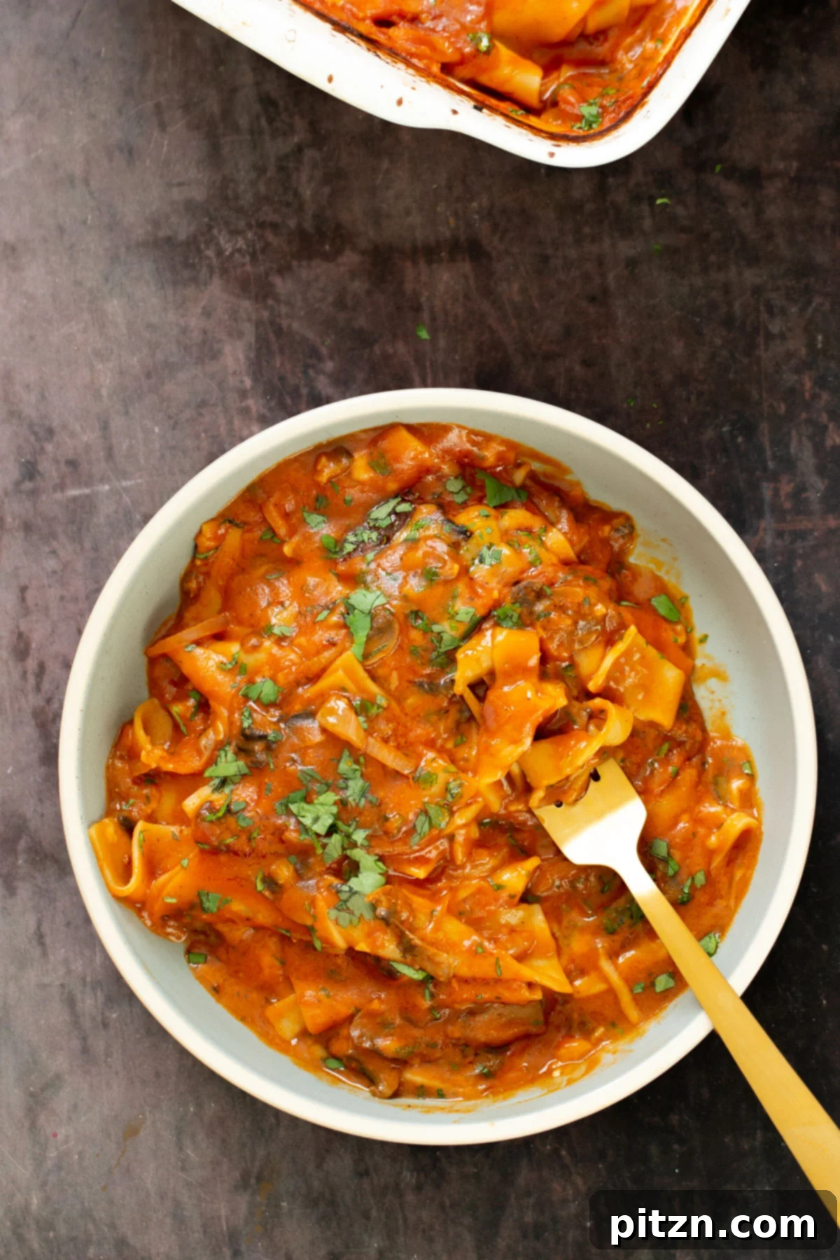 A beautiful serving of vegan butter chicken lasagna bake in a white bowl with a fork, showing the rich sauce and pasta layers.