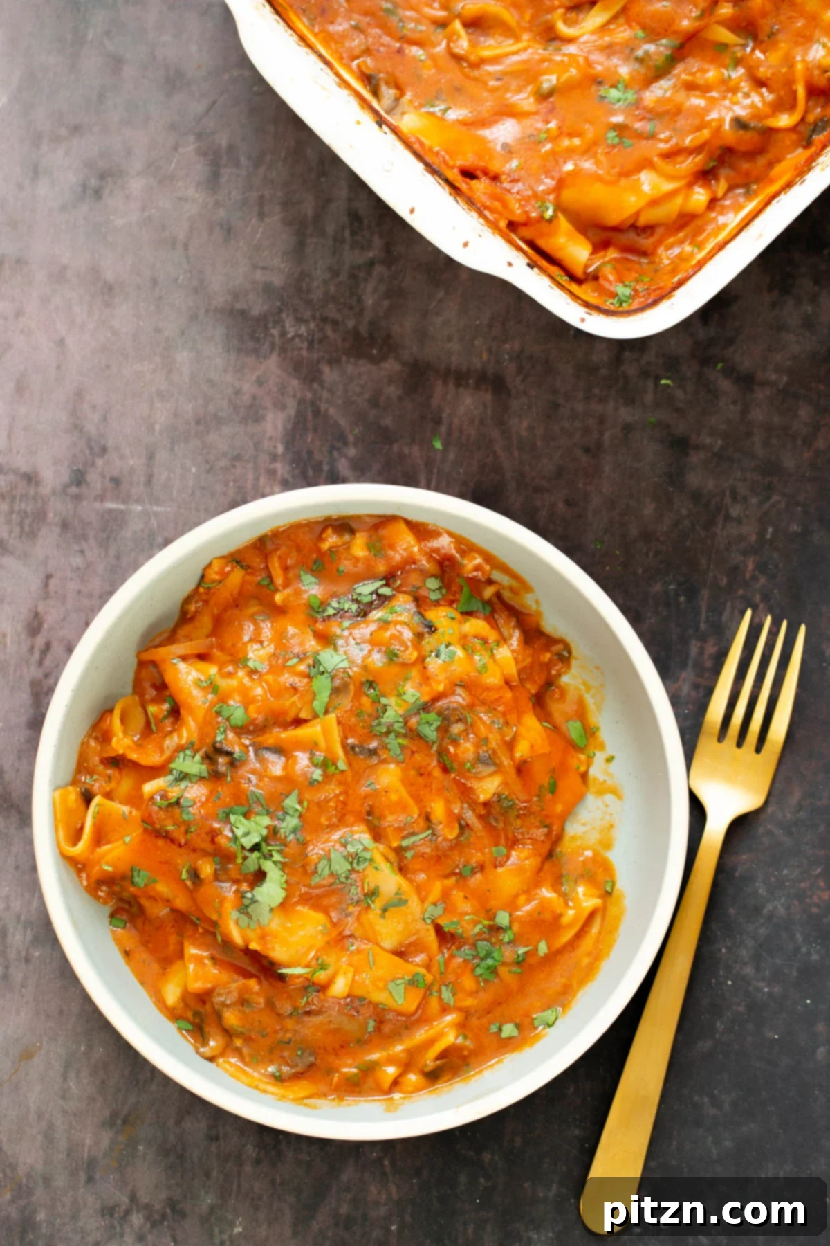 A bowl of vegan butter chicken lasagna next to a casserole dish filled with more lasagna, showcasing the finished dish.