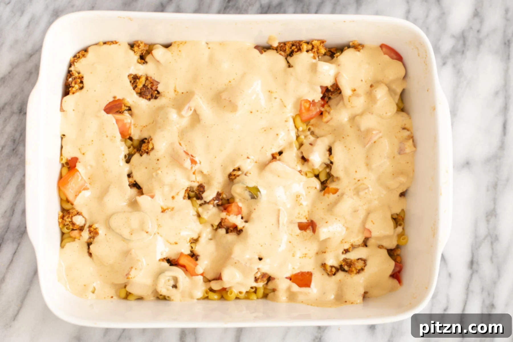 vegan queso sauce being poured over mac and cheese taco casserole