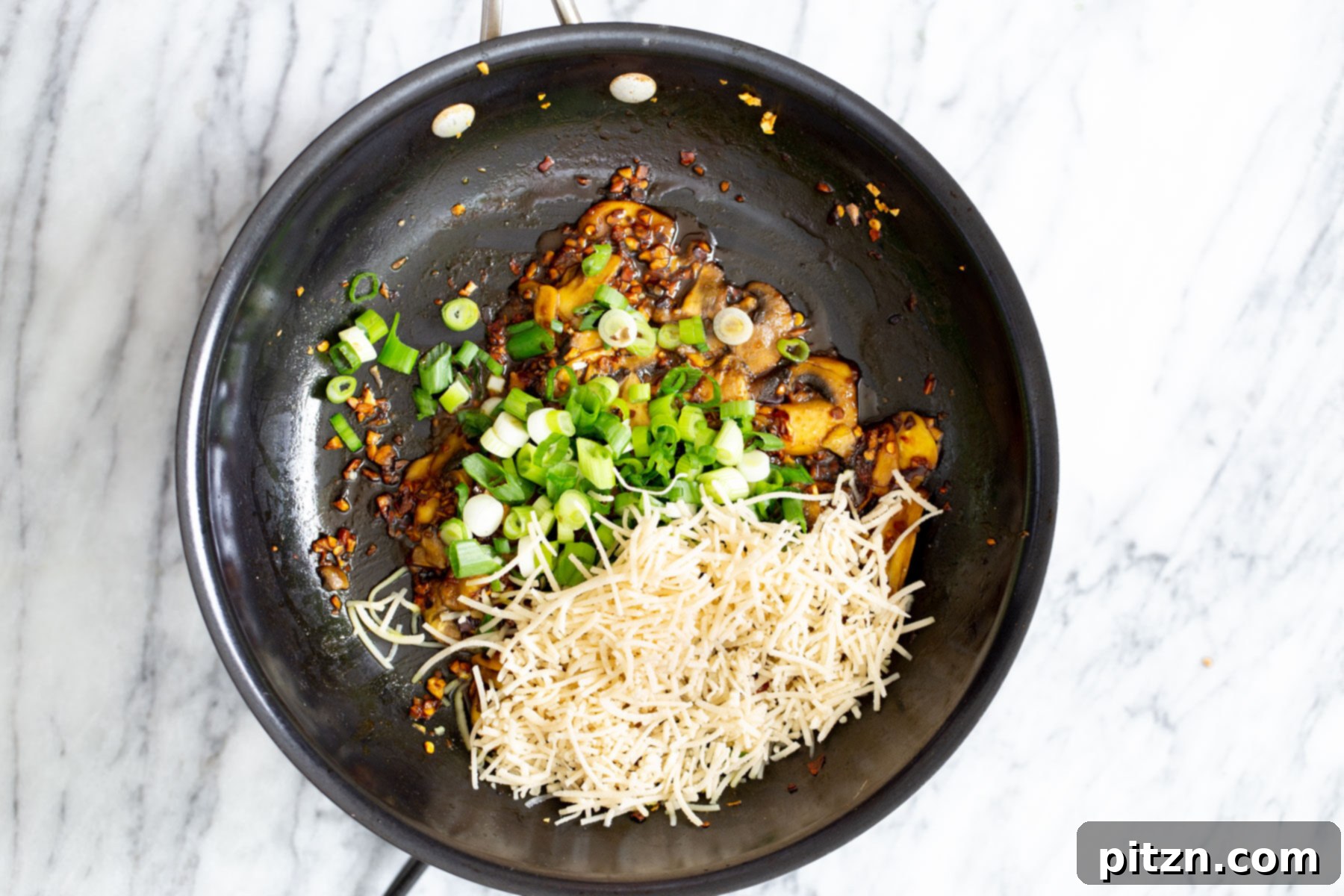 Ultimate Vegan Garlic Noodles 4 A vibrant mix of garlic, mushrooms, fresh scallions, and vegan Parmesan cheese is tossed together in a pan, ready to be combined with pasta for a quick and flavorful vegan dish.