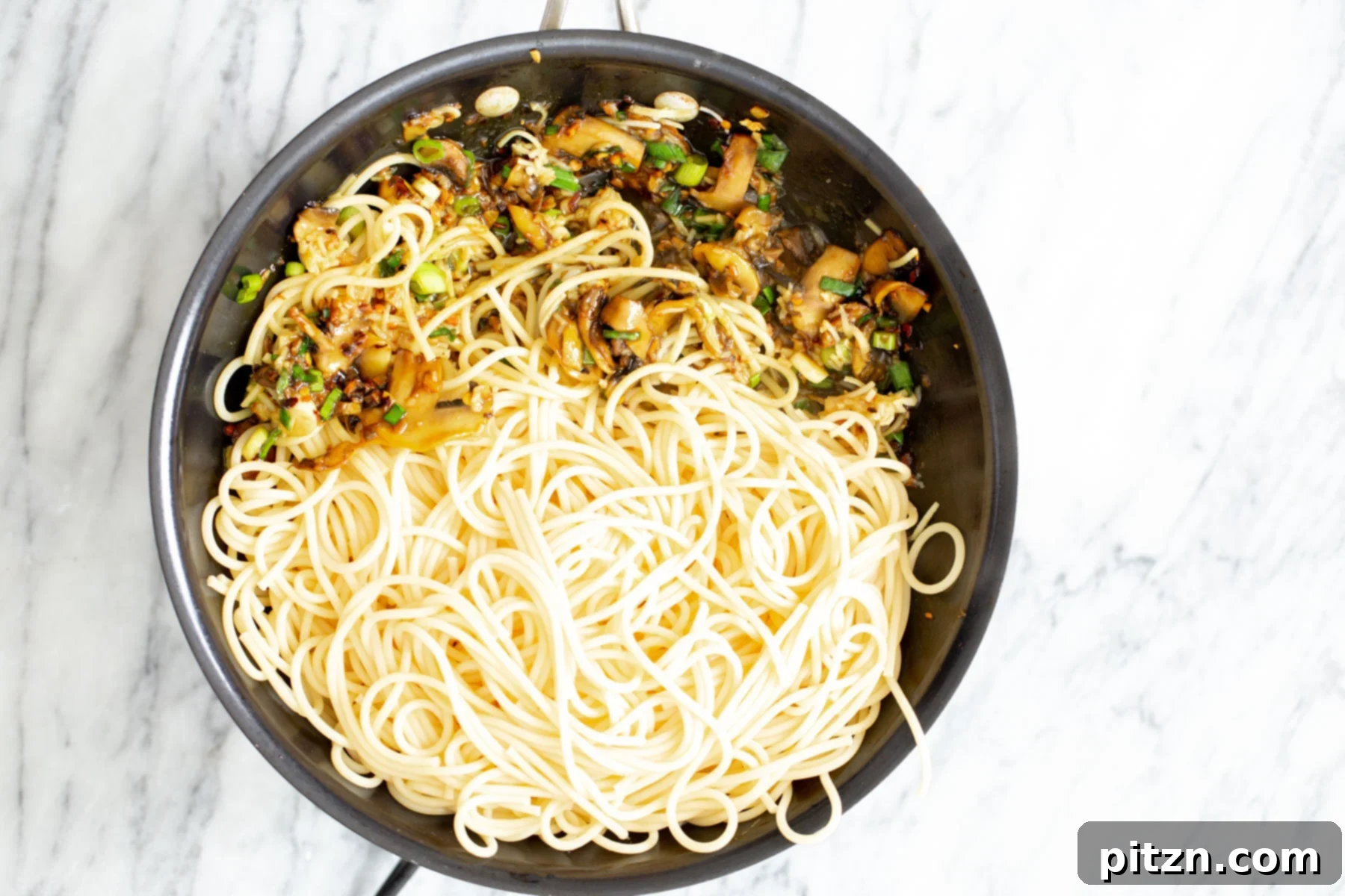 Ultimate Vegan Garlic Noodles 5 Cooked pasta is gently being added to a pan brimming with sautéed mushrooms, garlic, and scallions, preparing to be coated in the rich, savory sauce for a delicious garlic pasta.