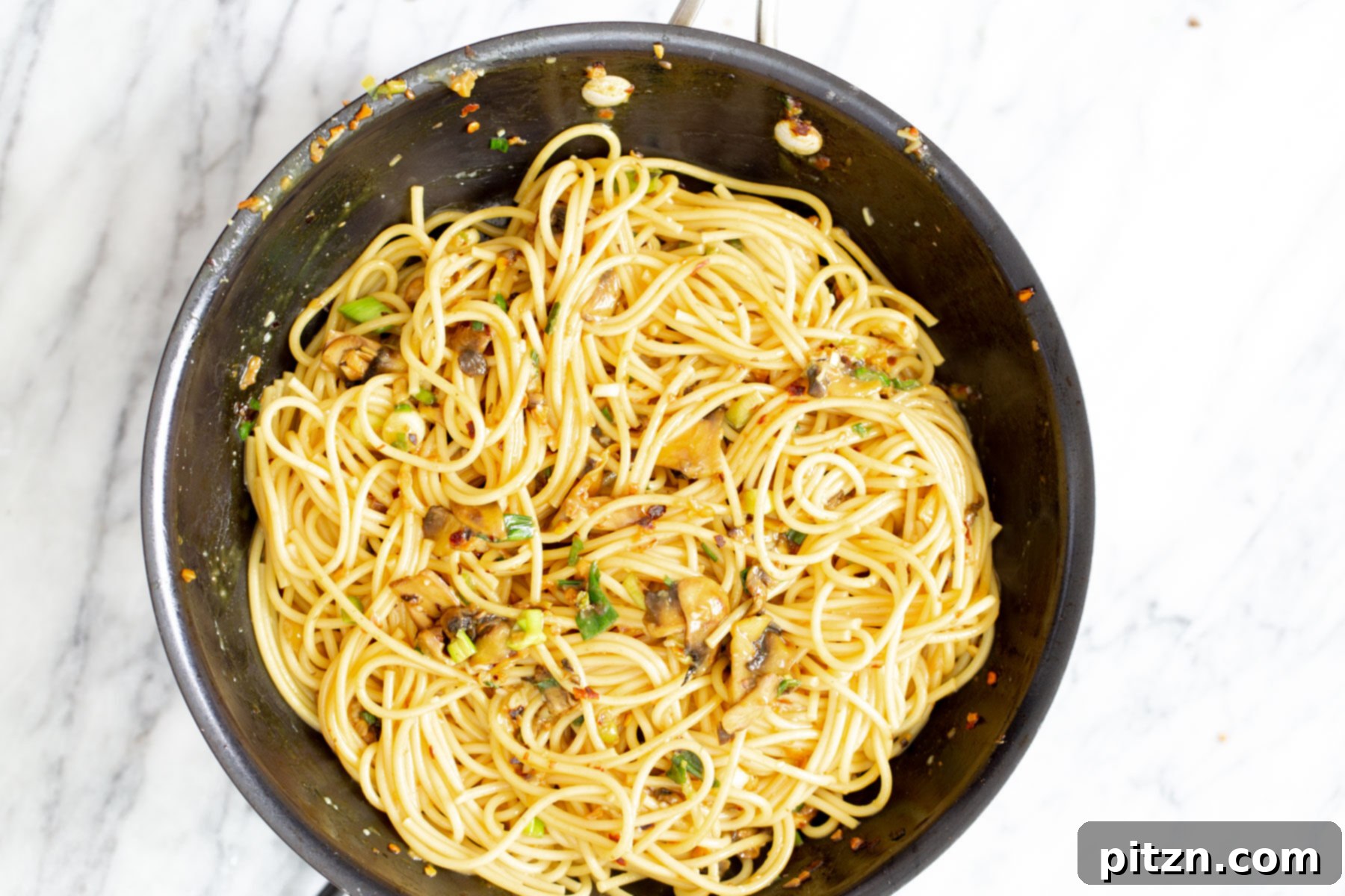Perfectly Tossed Vegan Garlic Pasta Vegan garlic pasta is being expertly tossed with pasta water in a sautéing pan, ensuring every noodle is perfectly coated in the rich, savory sauce, promising a delightful texture.