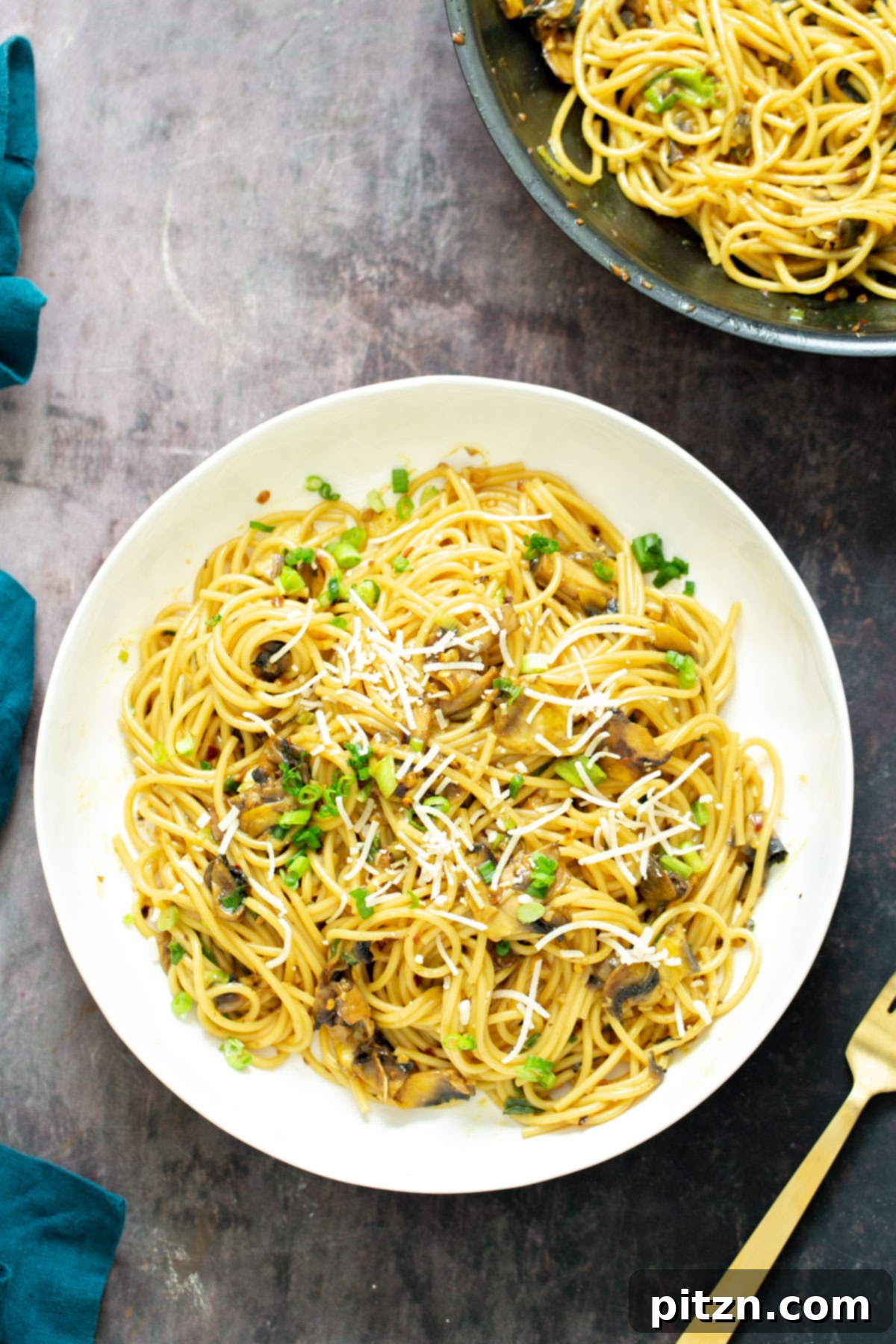 Exquisite Vegan Garlic Pasta Dish A close-up of a beautifully presented plate of vegan garlic pasta, generously topped with freshly chopped green onions and a sprinkle of grated vegan Parmesan cheese, ready for enjoyment.