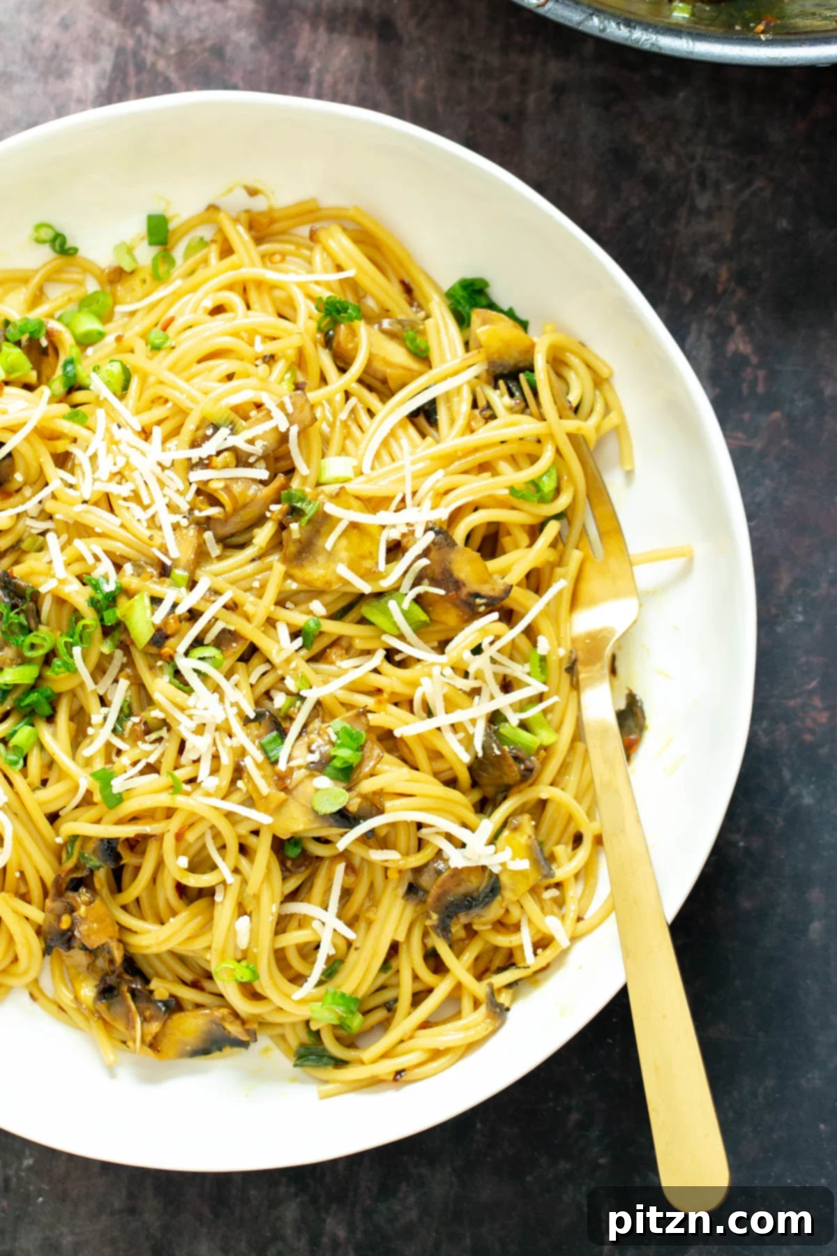 Irresistible Vegan Garlic Pasta Close-up of a plate of savory vegan garlic pasta, generously topped with grated vegan Parmesan cheese and freshly chopped scallions, showcasing its rich texture.
