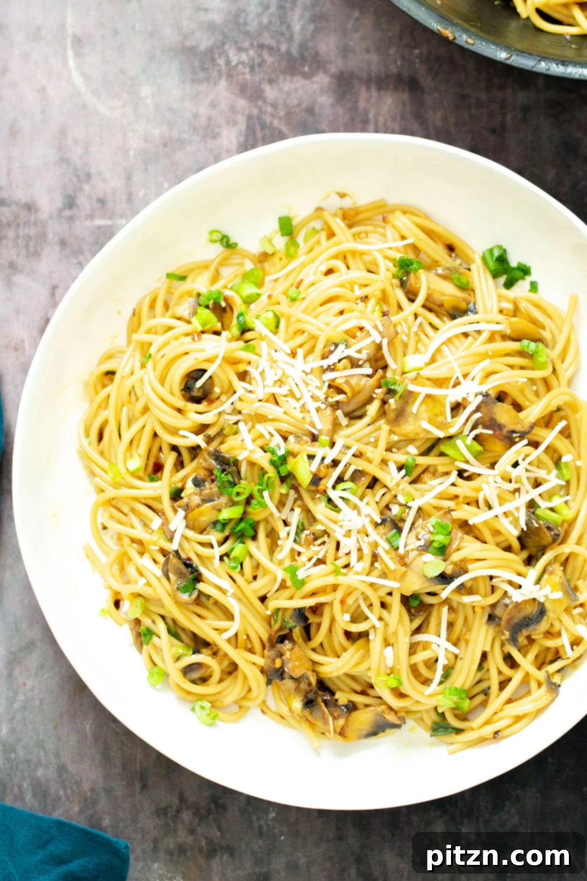 Hearty Vegan Garlic Pasta with Mushrooms A vibrant plate of vegan garlic pasta featuring mushrooms, artfully garnished with a sprinkle of vegan Parmesan and fresh scallions, promising a delightful culinary experience.