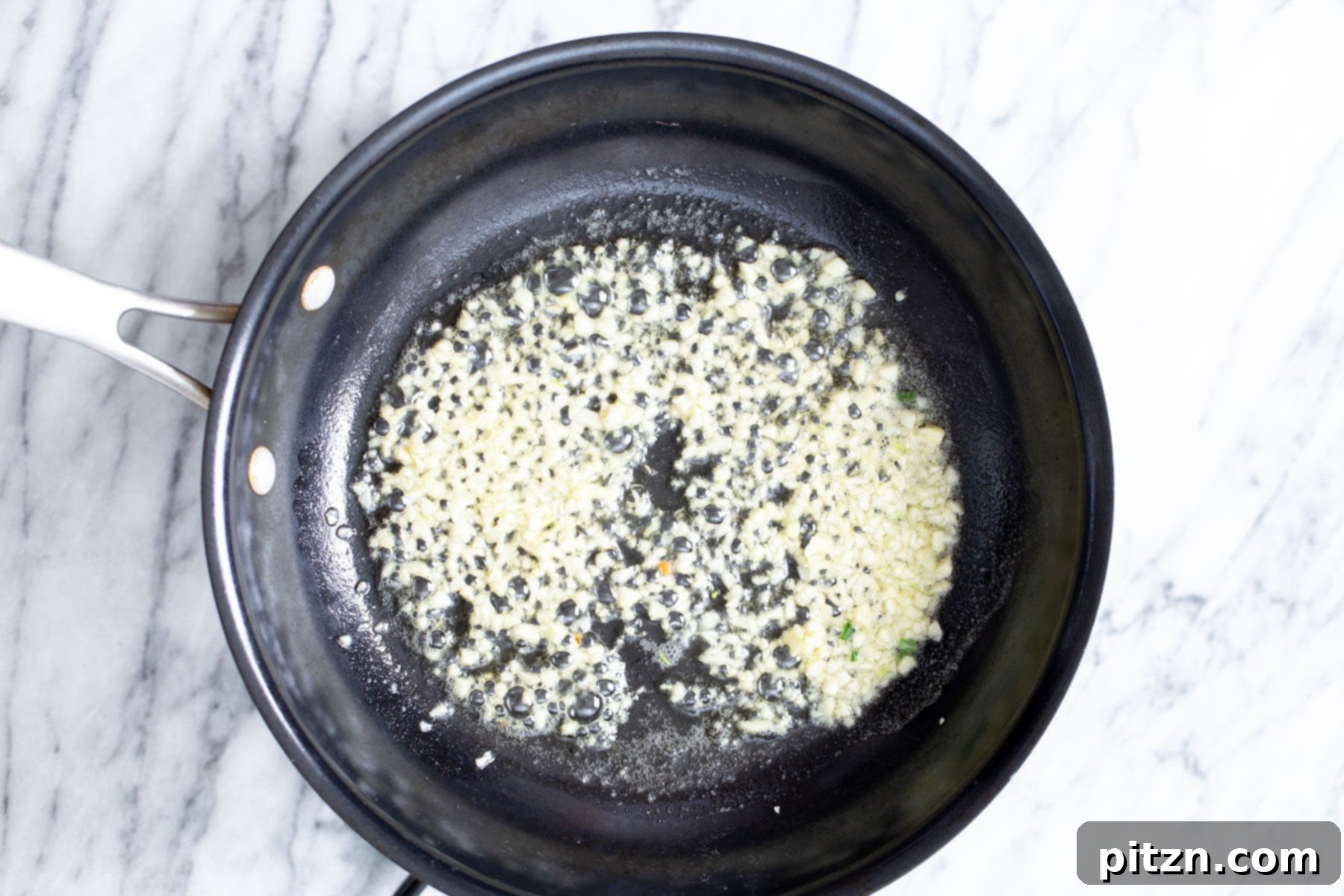 Ultimate Vegan Garlic Noodles 3 Minced garlic cloves are being gently fried in a pan with hot oil, turning golden and aromatic, ready to form the flavorful base for garlic noodles.