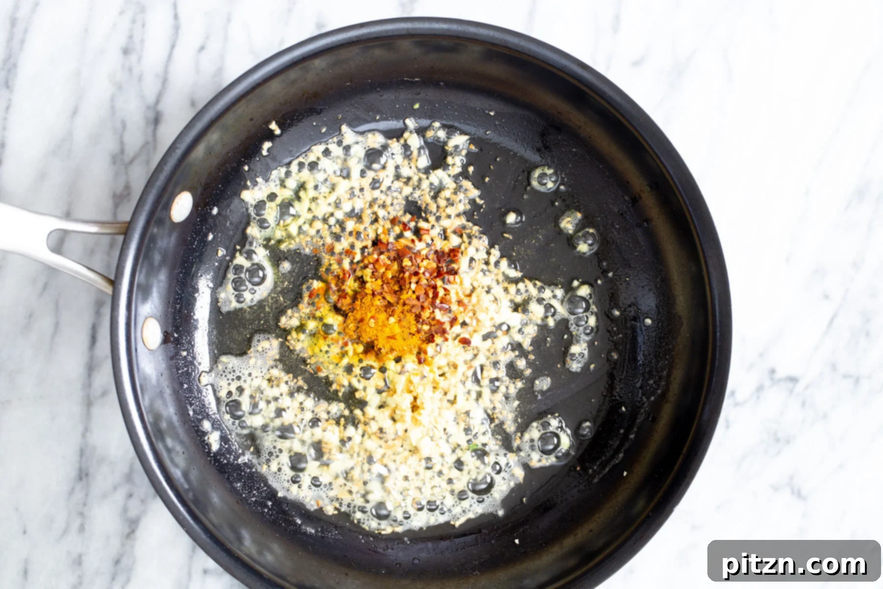Garlic Pasta Flavor Boost A mix of turmeric and vibrant red pepper flakes are being sprinkled into a hot frying pan containing sautéed garlic, creating an aromatic and colorful base for a delicious garlic pasta sauce.