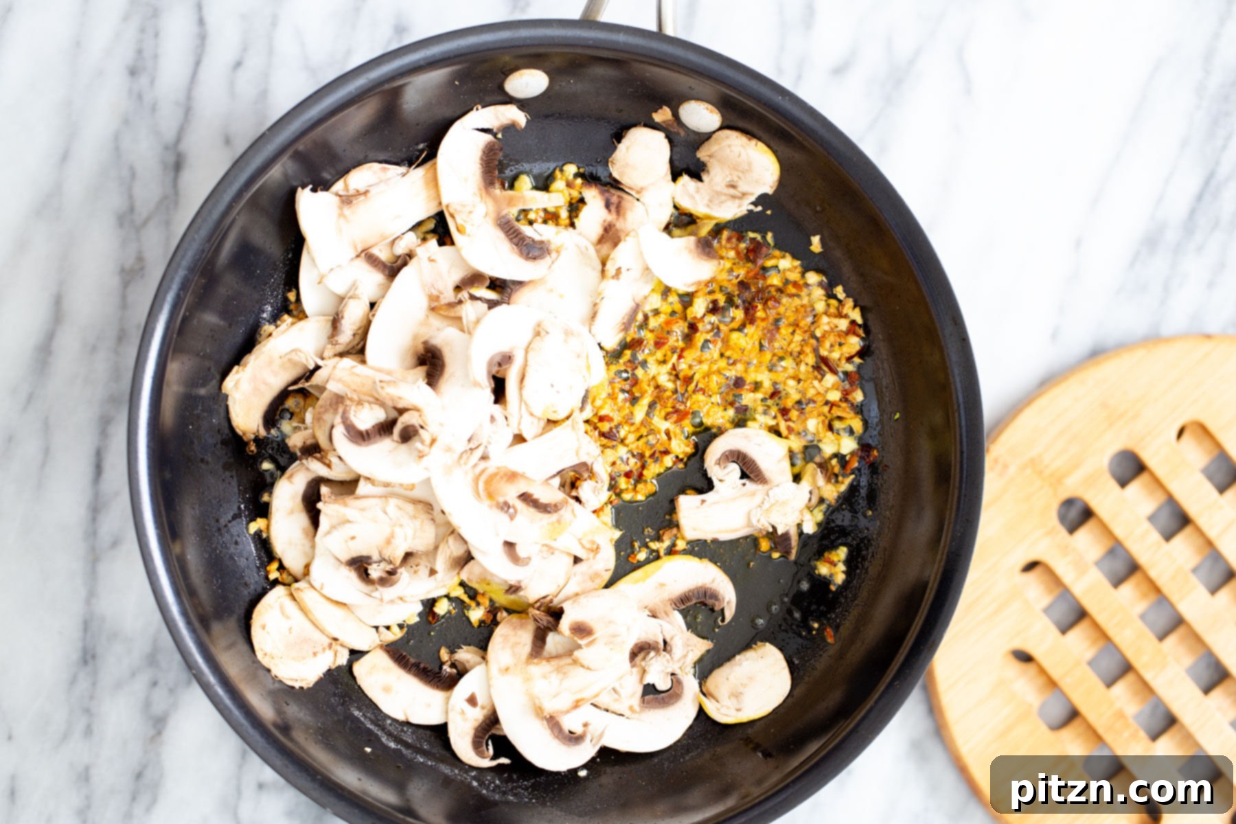 Vegan Garlic Pasta with Mushrooms Thinly sliced mushrooms are being added to a pan of fragrant sautéed garlic, starting to cook down and absorb the delicious flavors for a vegan garlic pasta.