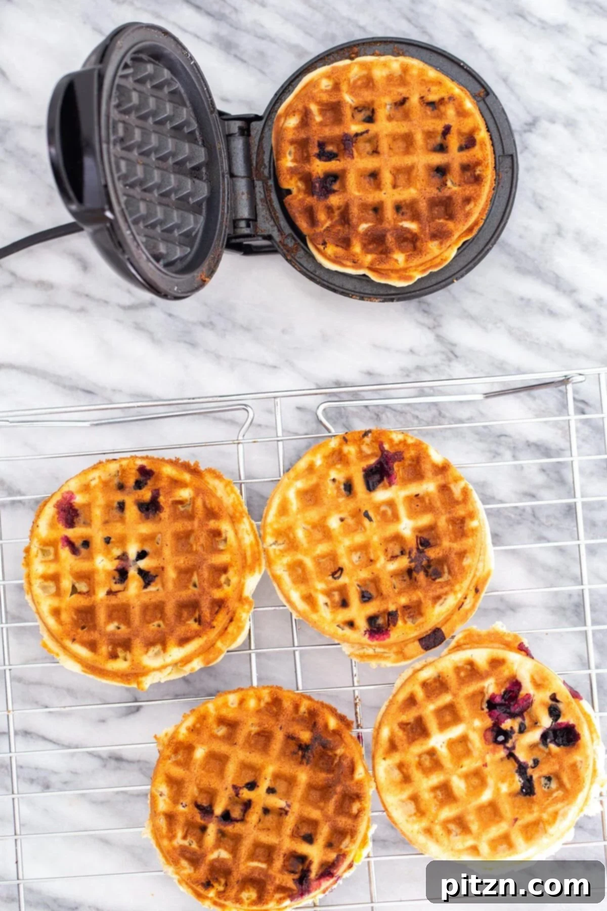 Freshly baked vegan gluten-free lemon blueberry waffles cooling on a wire rack, showcasing their perfectly golden and crispy texture, ready to be enjoyed.