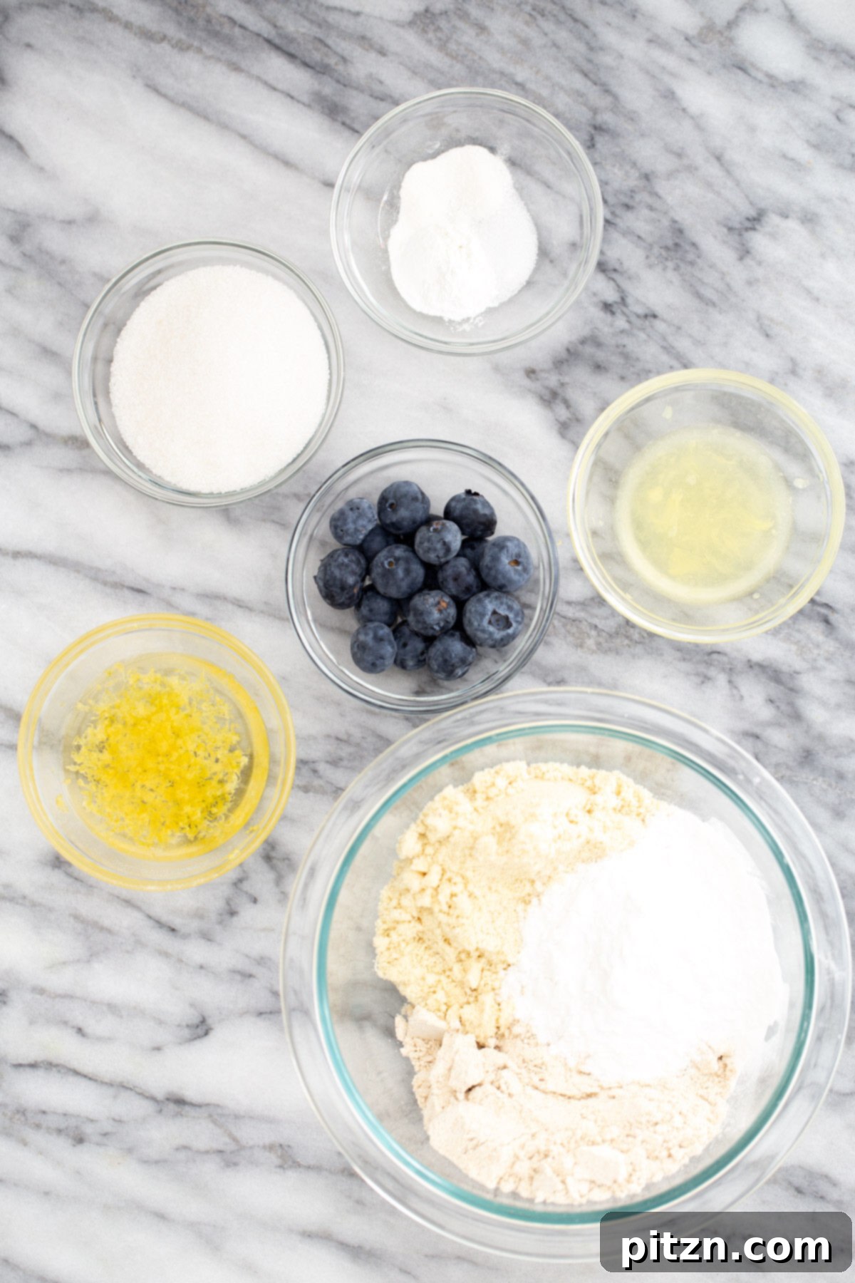 A collection of essential ingredients neatly arranged, ready for preparing gluten-free vegan lemon blueberry waffles, including flours, baking powder, lemon, blueberries, and oil.