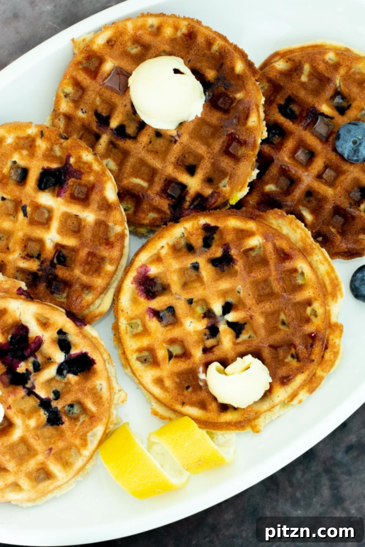 A stunning close-up of vegan gluten-free Lemon Blueberry Waffles artfully arranged on a platter, adorned with tantalizing dollops of vegan butter, inviting you to indulge in a delightful breakfast.