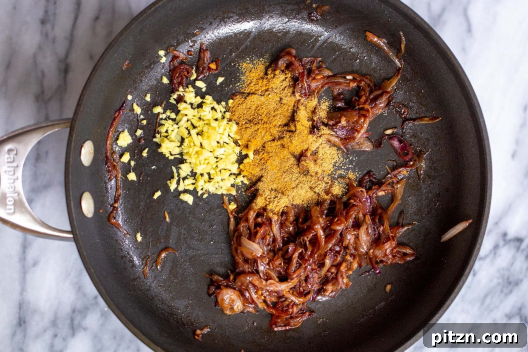 dried spices and ginger being added to sauteed onions in sauteeing pan