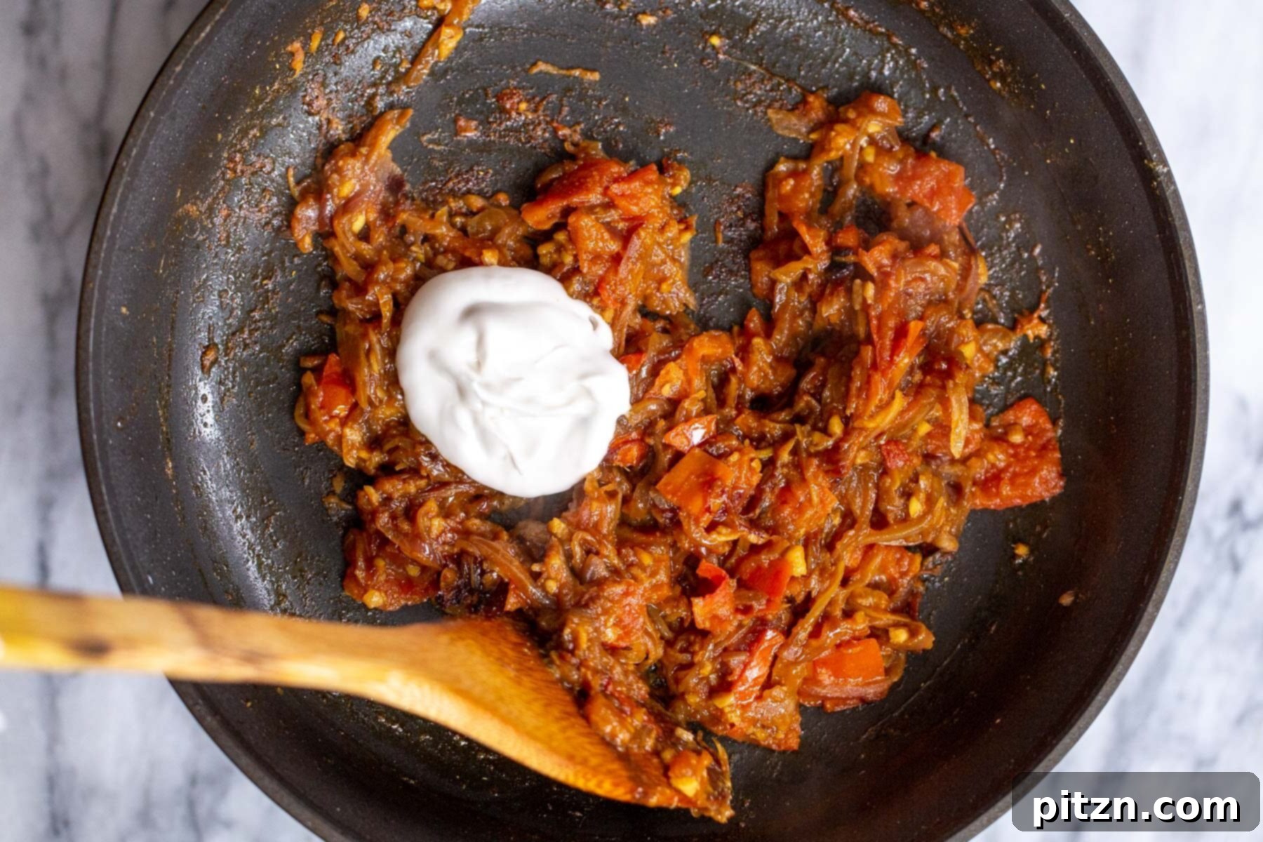 coconut yogurt being added to tempered onions and spices in sauteeing pan