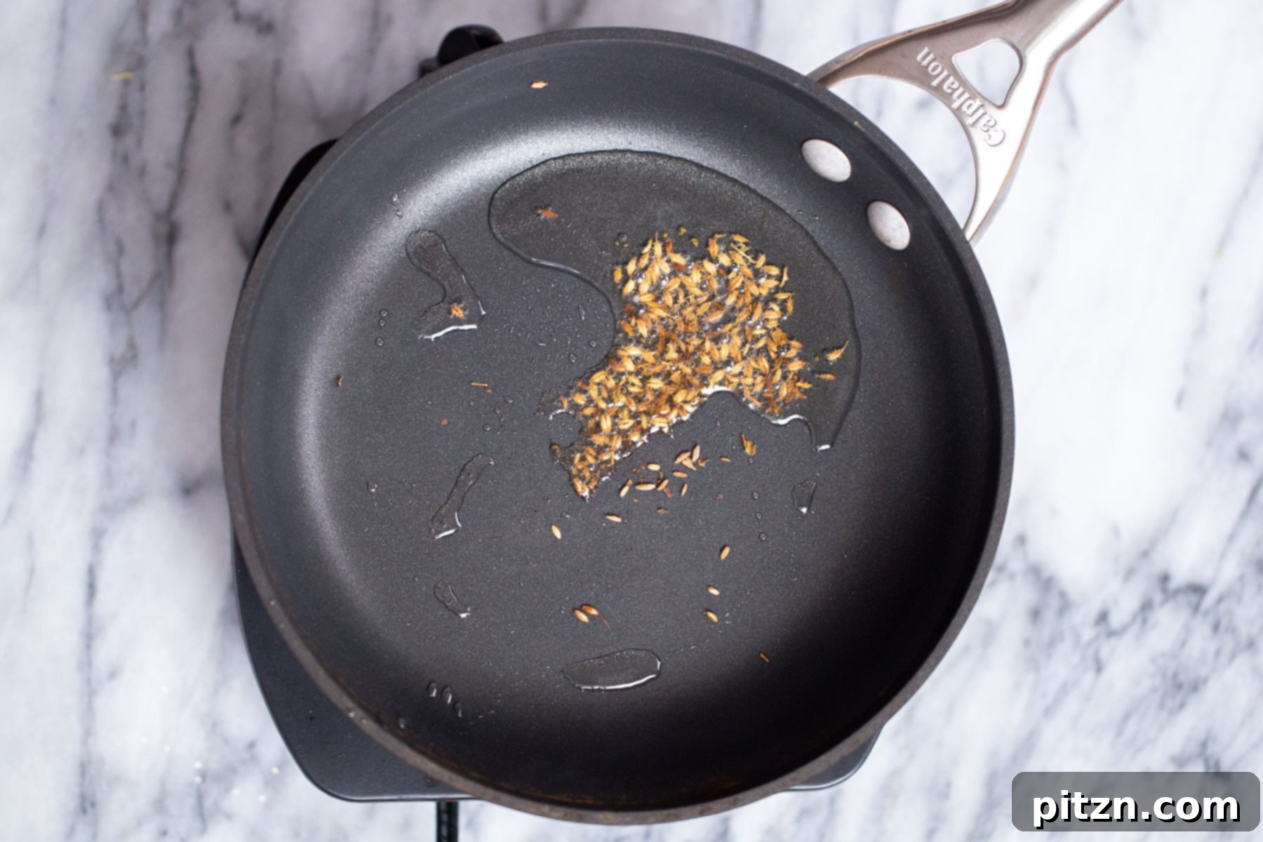 cumin seeds being added to hot oil in a sauteeing pan 
