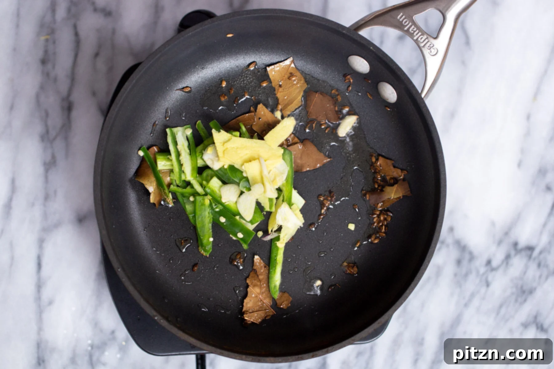 ginger and green chile being added to sauteeing pan with hot oil 