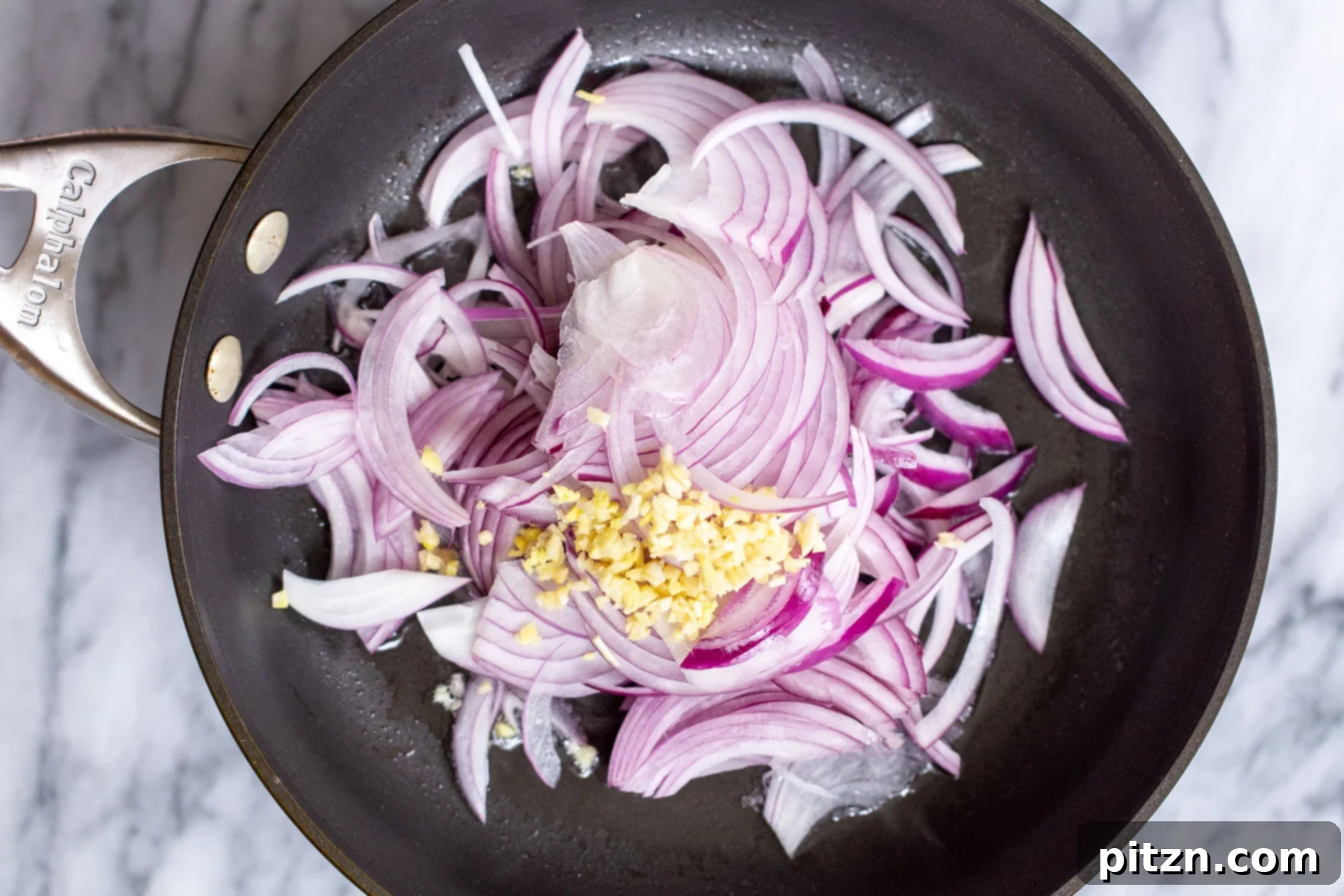 sliced red onions and ginger in a black sauteeing pan 