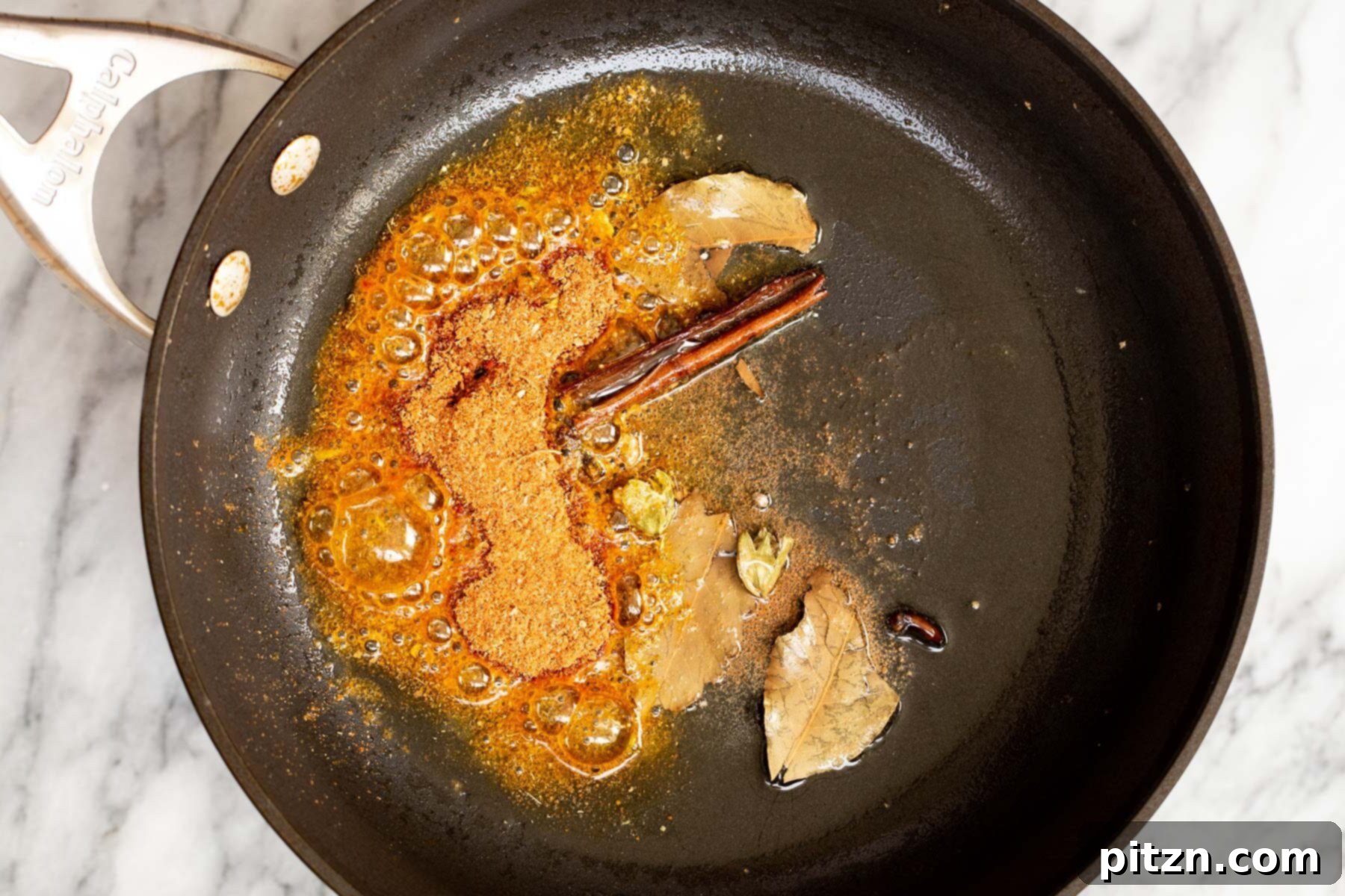 Vegan Tofu Rogan Josh 14 A mix of whole spices and ground spices sautéing together in hot oil within a skillet, creating an aromatic blend.