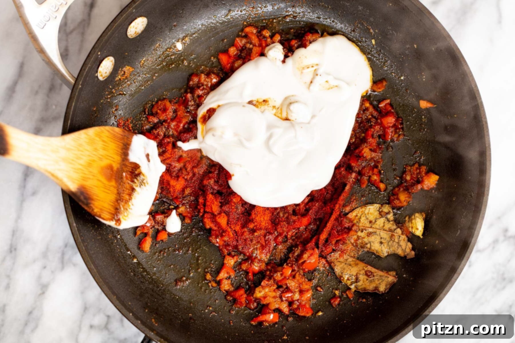 Vegan Tofu Rogan Josh 18 Unsweetened coconut yogurt being stirred into the simmering spices and bell pepper mixture in a sauté pan.