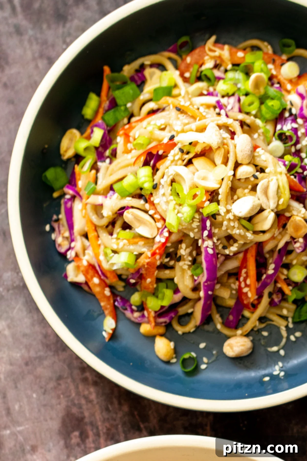 peanut sesame noodle salad with vegetables sprinkled with sesame seeds and peanuts in a serving bowl