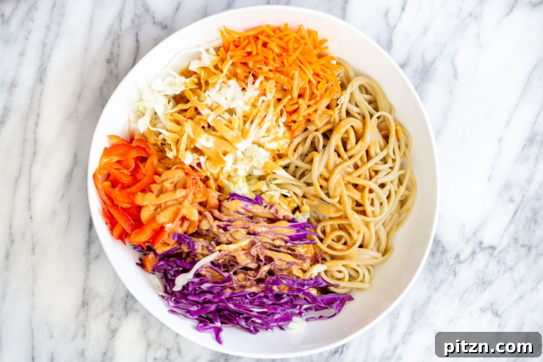peanut sesame noodle salad with chopped veggies drizzled with peanut butter dressing in a large bowl