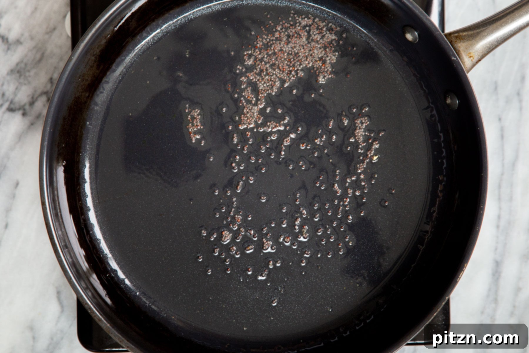 Hearty Vegan Malabar Curry 11 Mustard seeds crackling and frying in hot oil in a black frying pan.